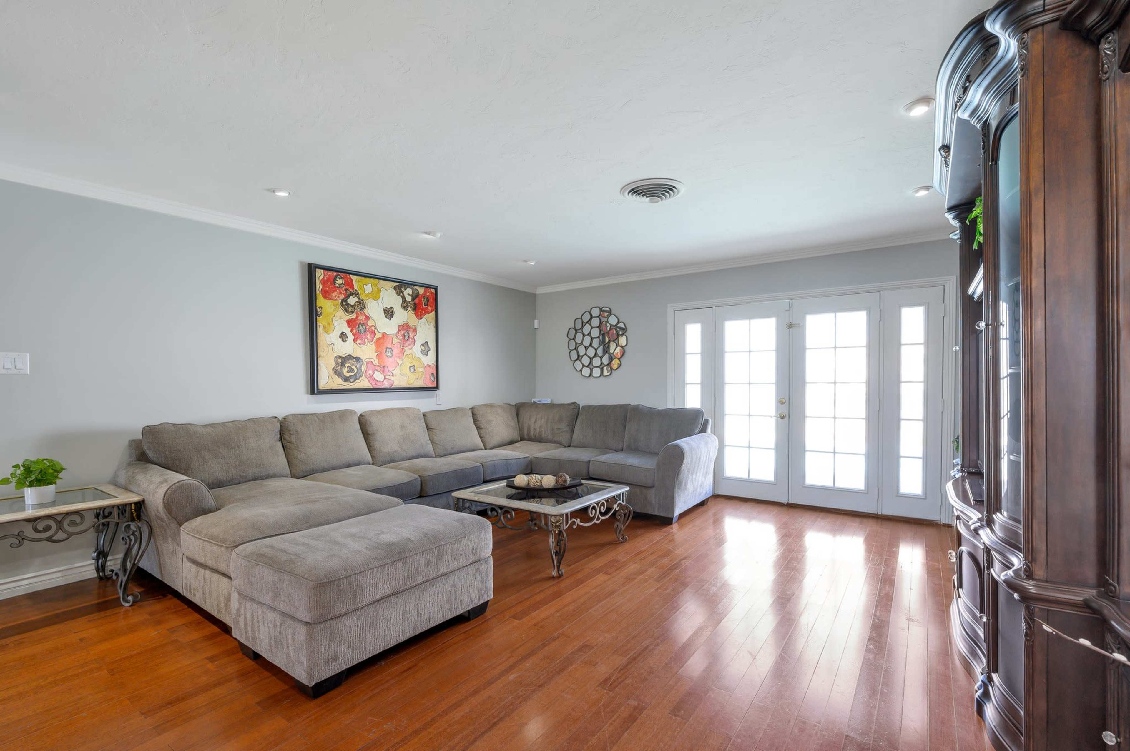 A spacious living room features a gray sectional sofa, a wooden coffee table, and French doors leading to an outdoor area.