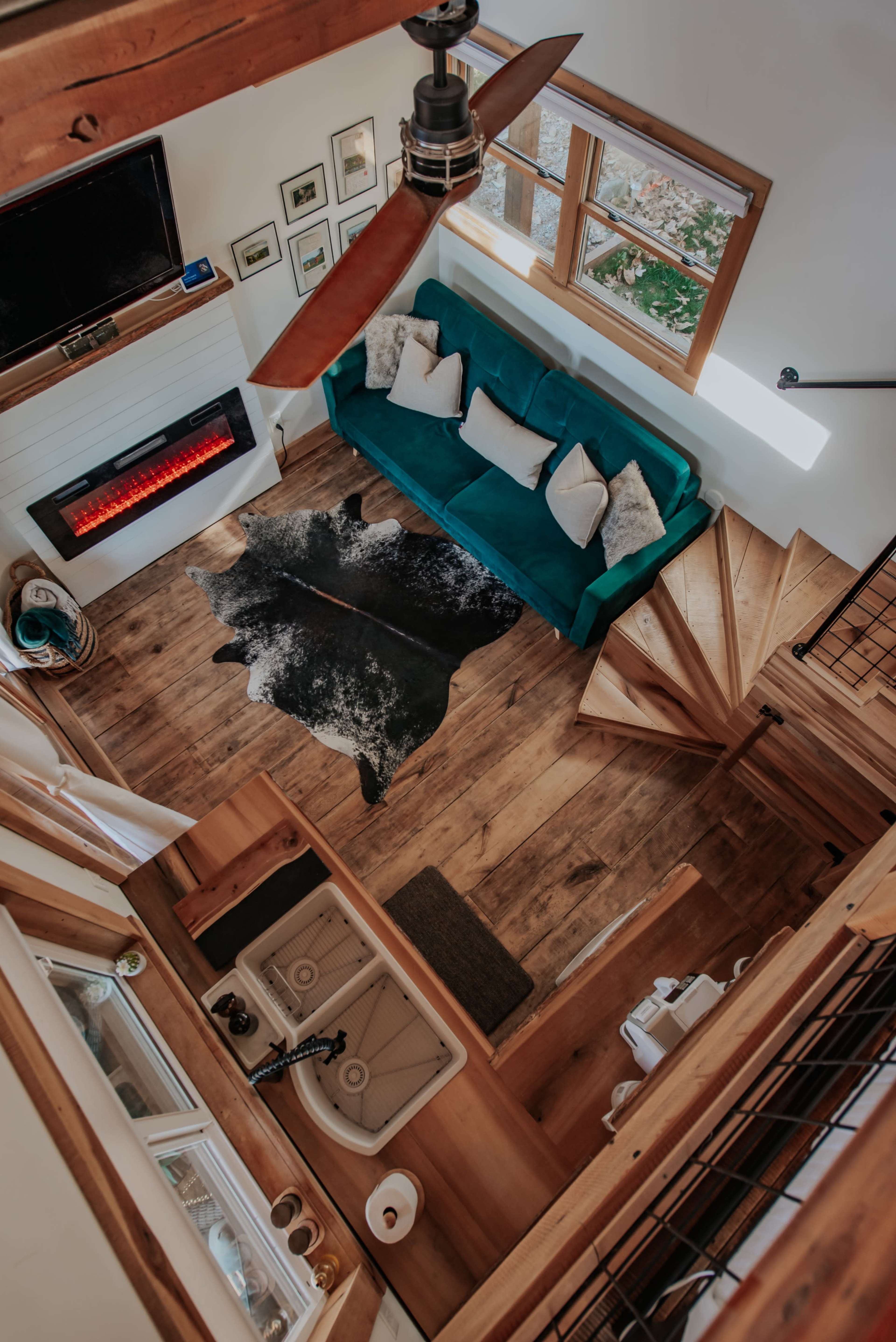 An interior space of a cozy multi-level home featuring a teal sofa, a cowhide rug on wooden flooring, a wall-mounted television, and an electric fireplace.