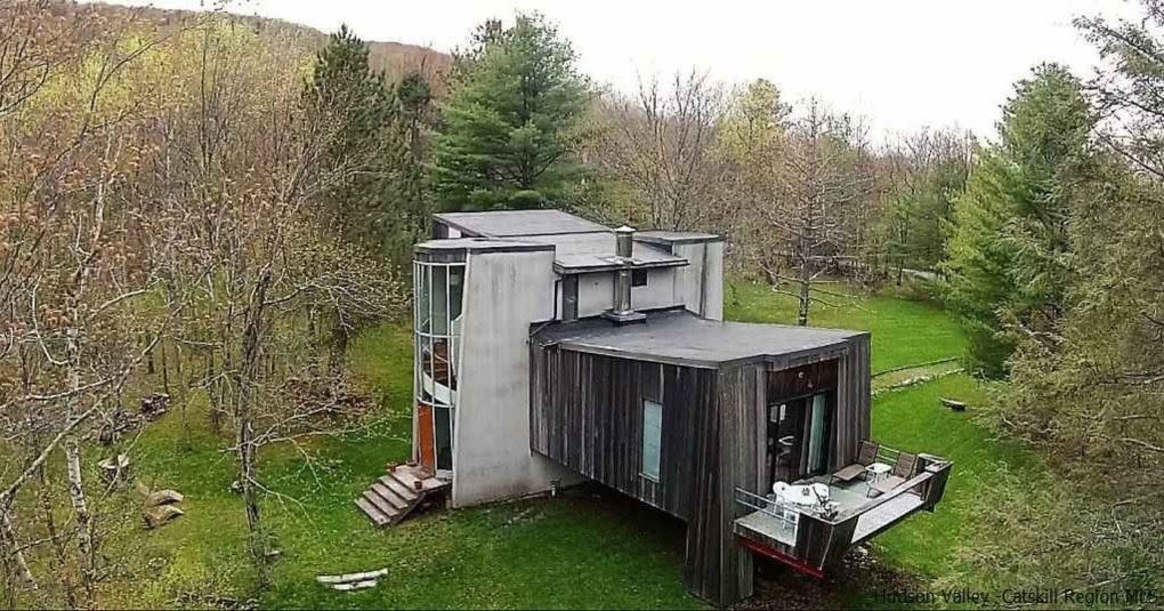 A modern, asymmetrical house with a mix of concrete and wooden exterior is situated in a wooded area.