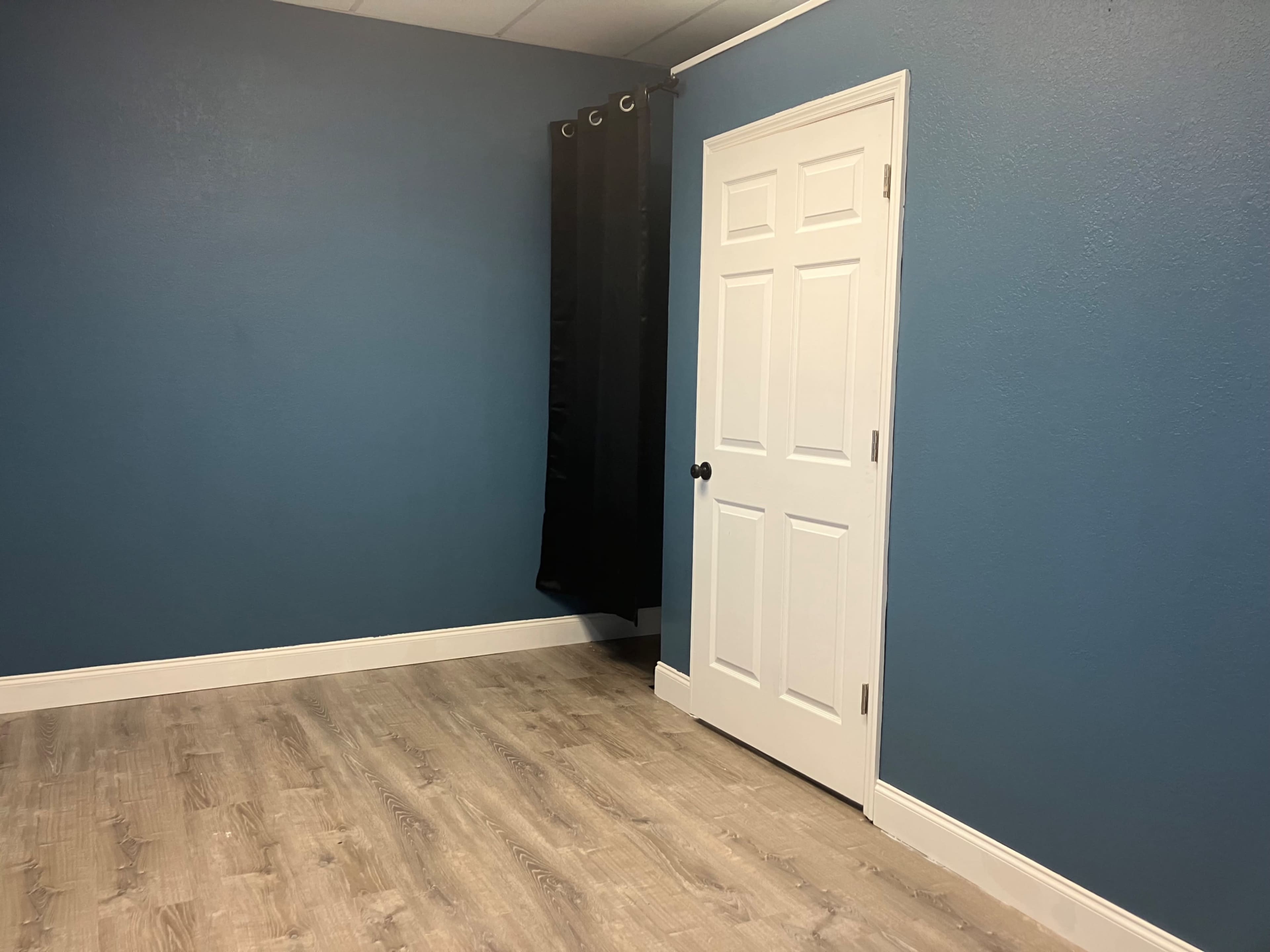 A room with blue walls, a white door, and a black curtain hanging in a corner.