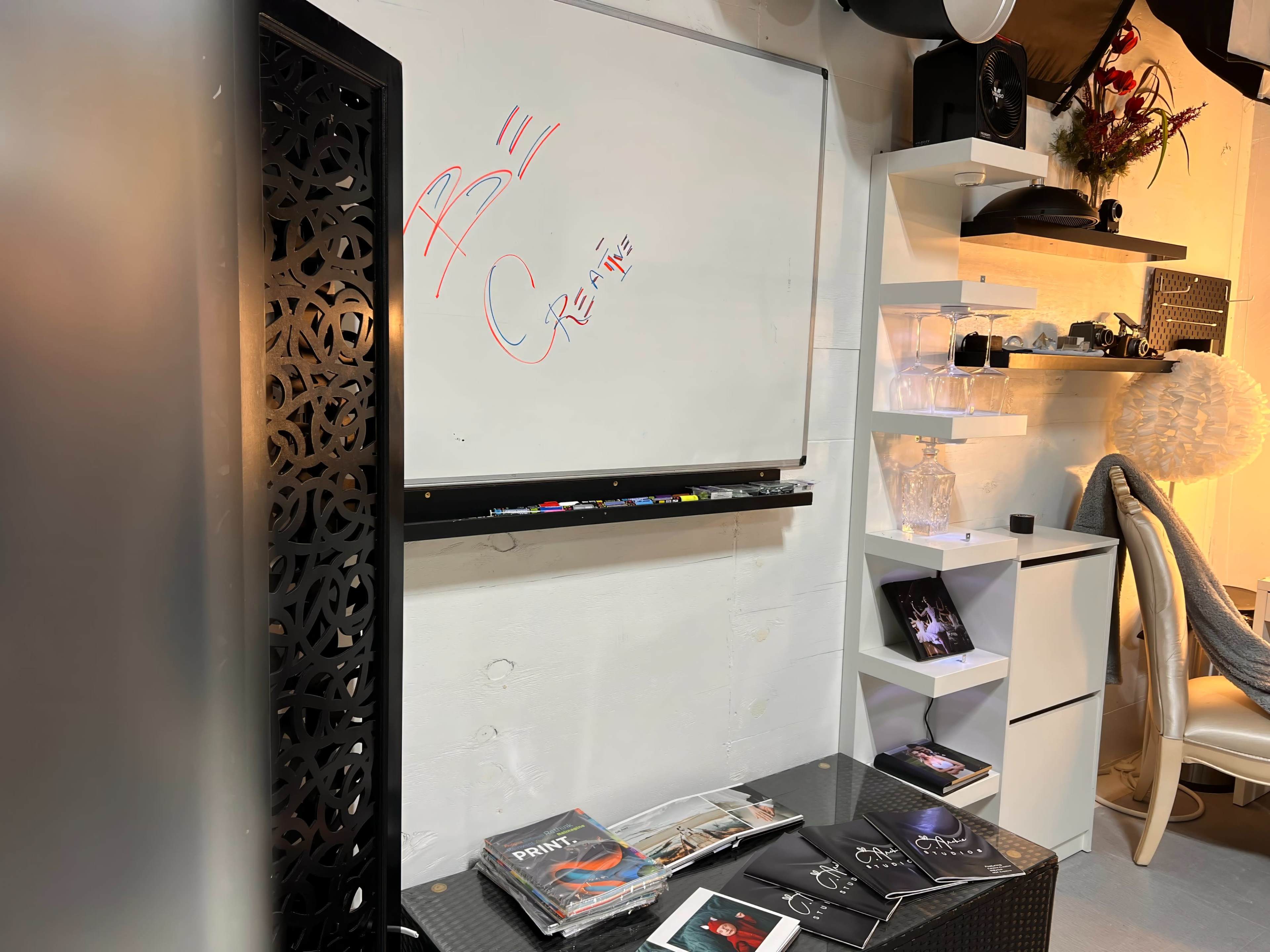 A whiteboard with red writing, a black decorative partition, and various items, including magazines and decorative pieces, arranged on shelves in a room.