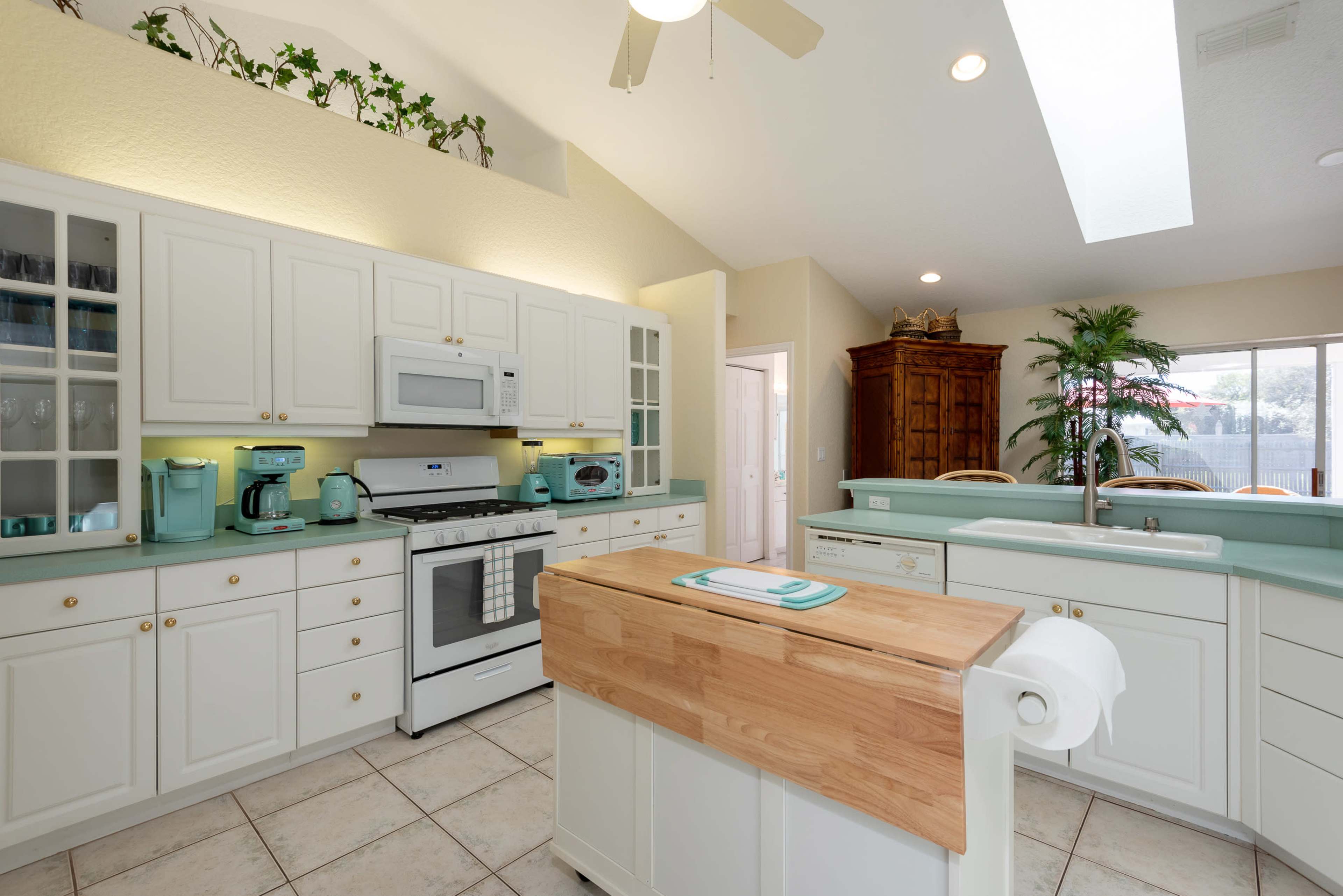 A modern kitchen features white cabinetry, a central wooden island, and light-colored countertops, with appliances in mint green and ample natural light.
