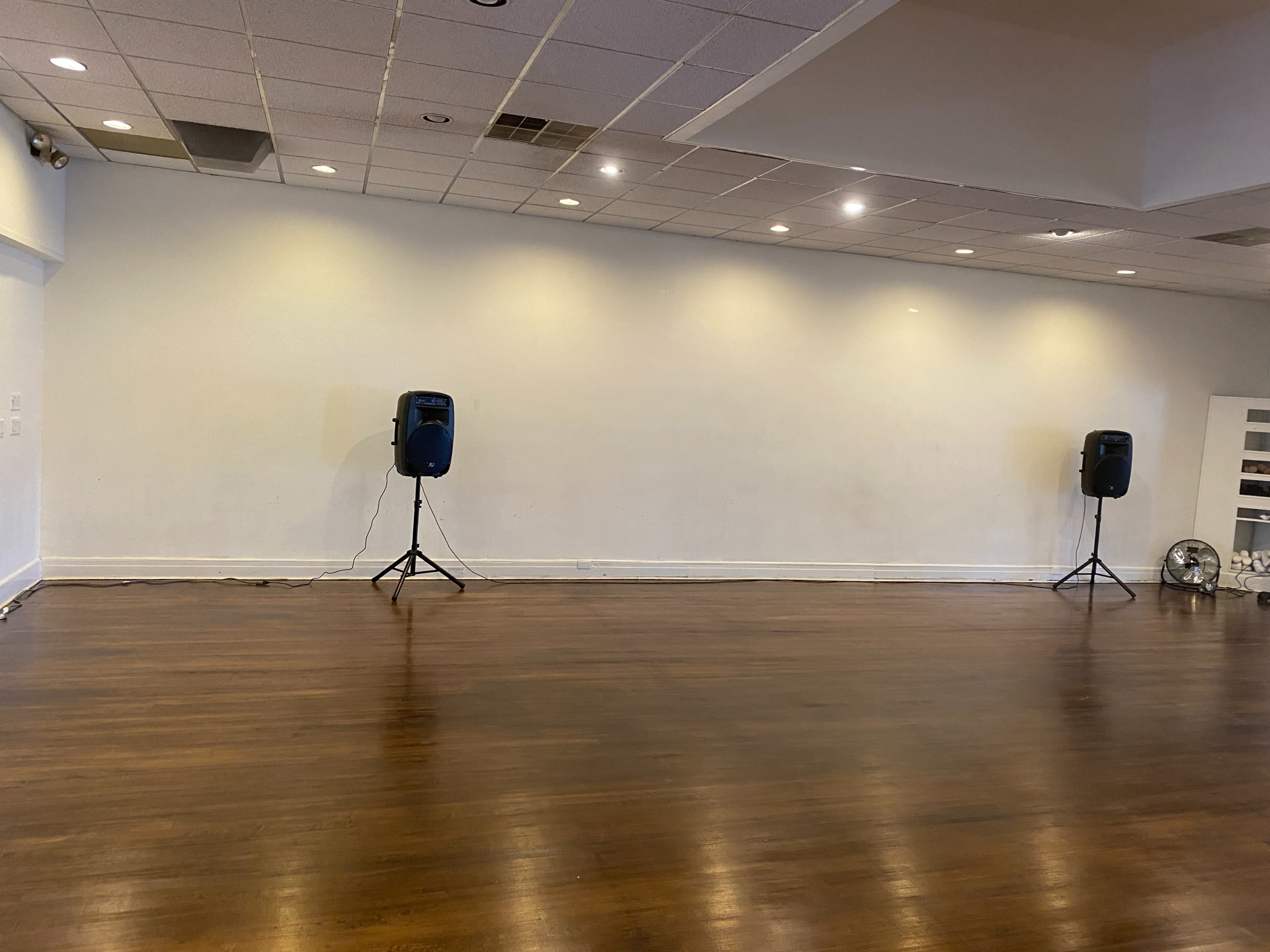 The image shows a spacious, empty room with two speaker stands positioned on either side against a blank wall.