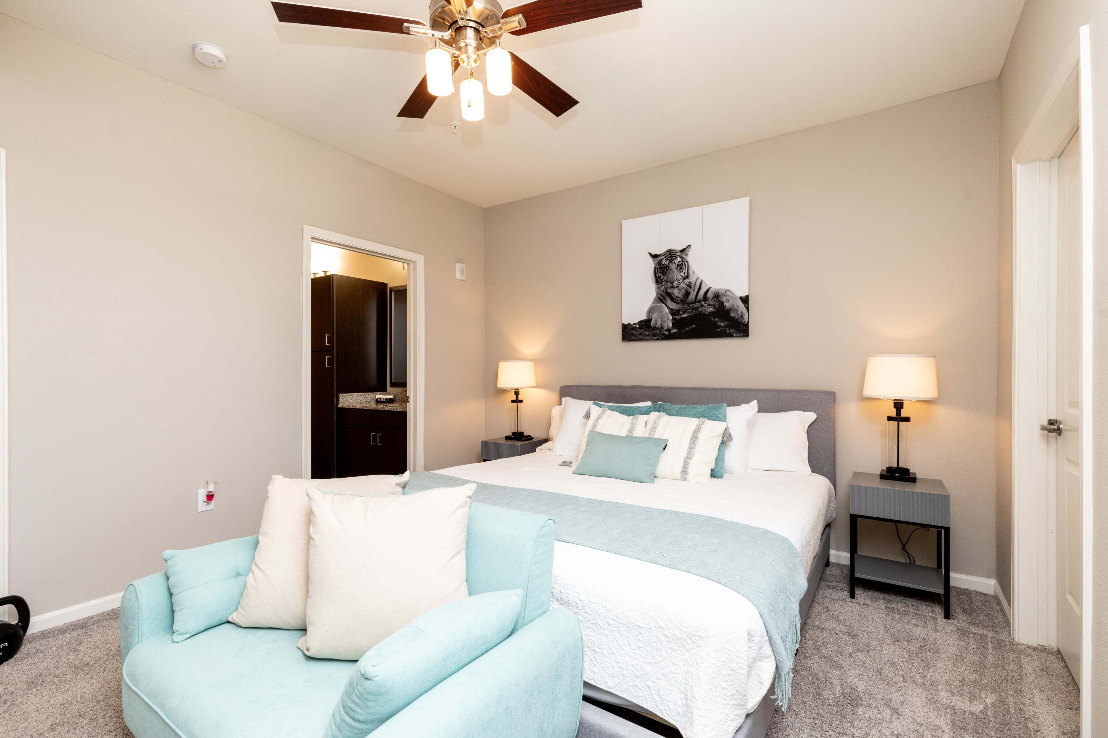 A bedroom with a king-sized bed, two nightstands with lamps, a small armchair, and a wall-mounted picture of a tiger.