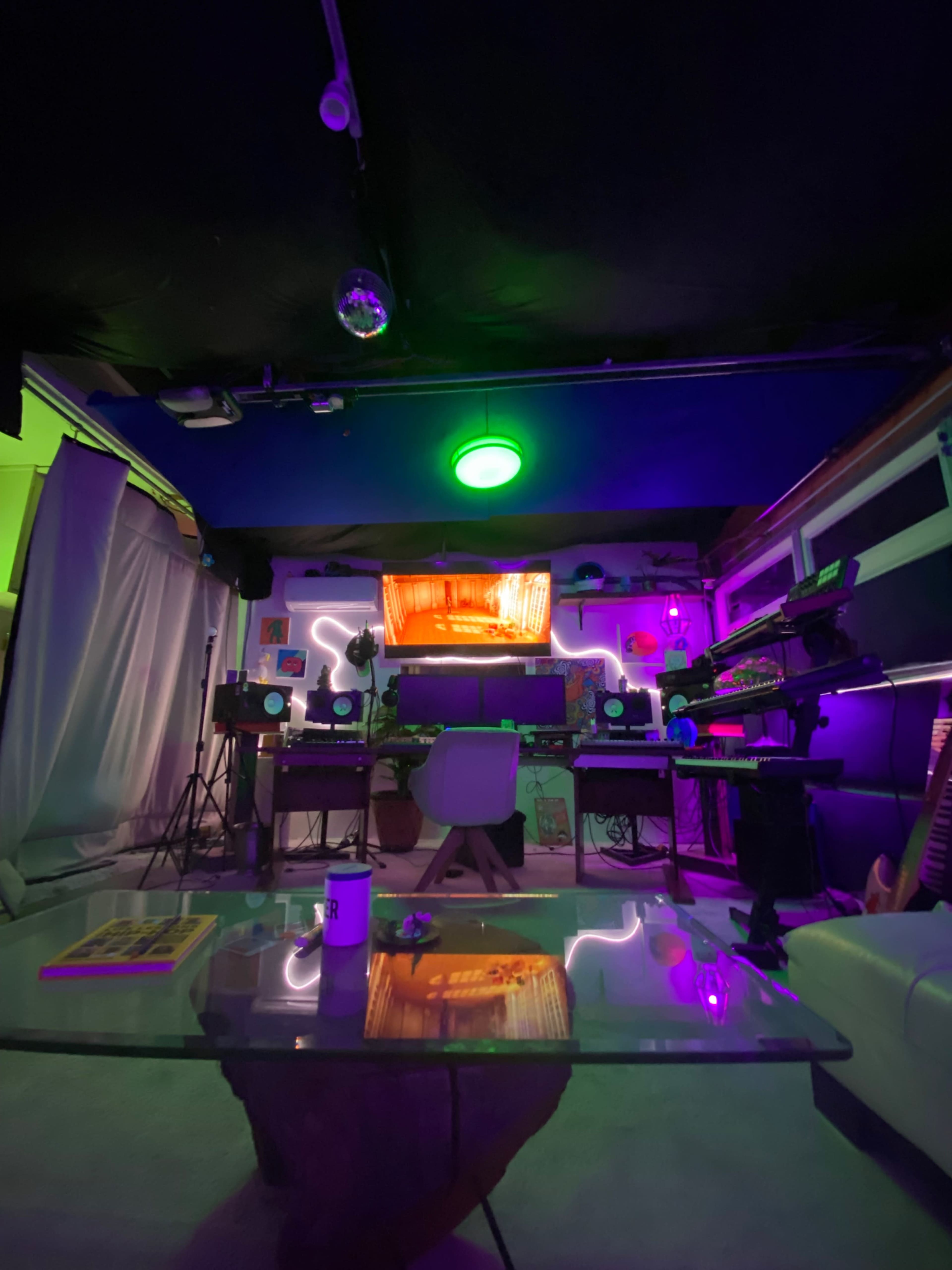 The image shows a vibrant music studio featuring colorful neon lights, a modern desk setup, and various musical equipment arranged around the room.