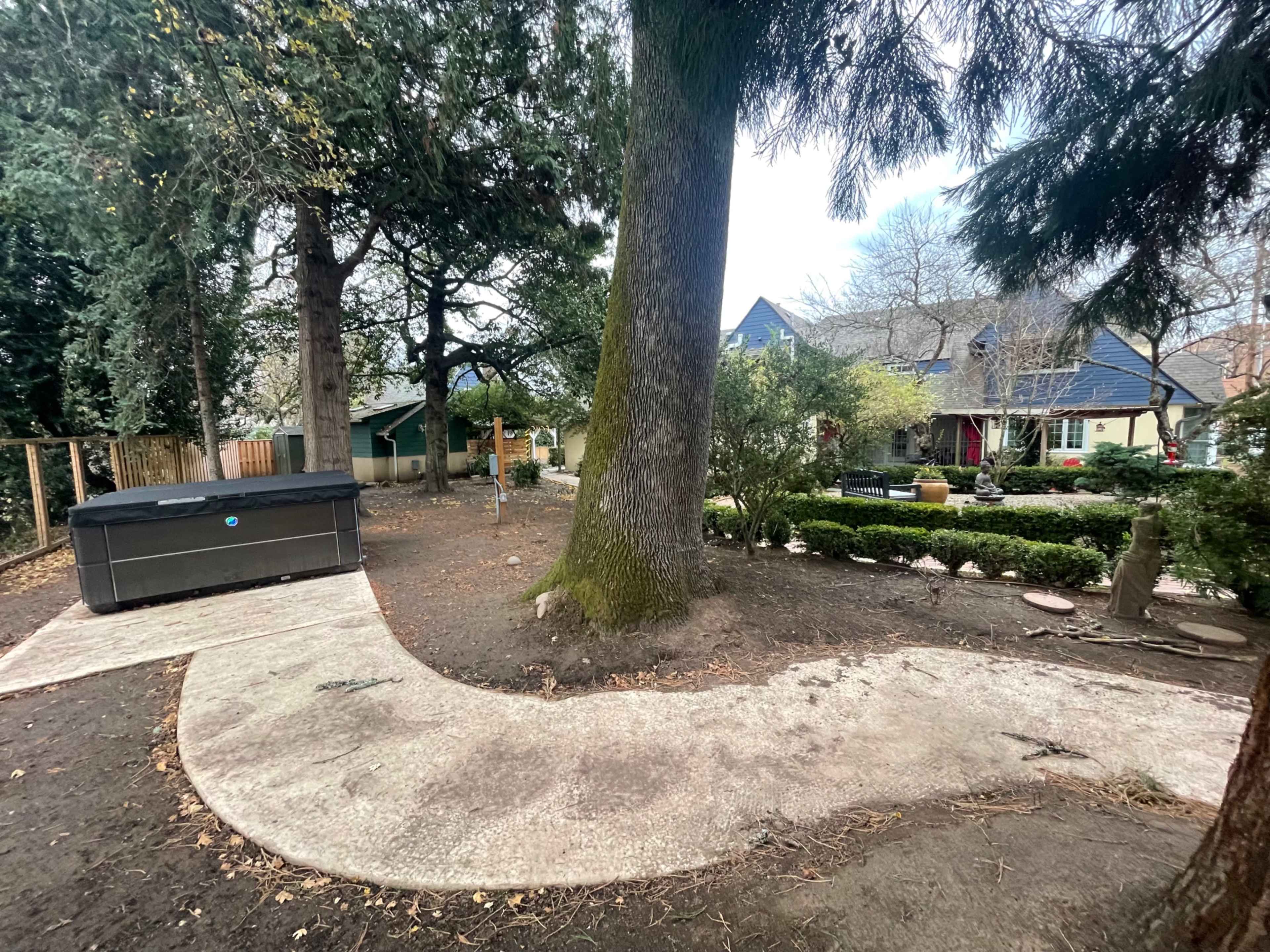 A curved concrete pathway leads through a landscaped yard with trees, a hot tub, and a house in the background.