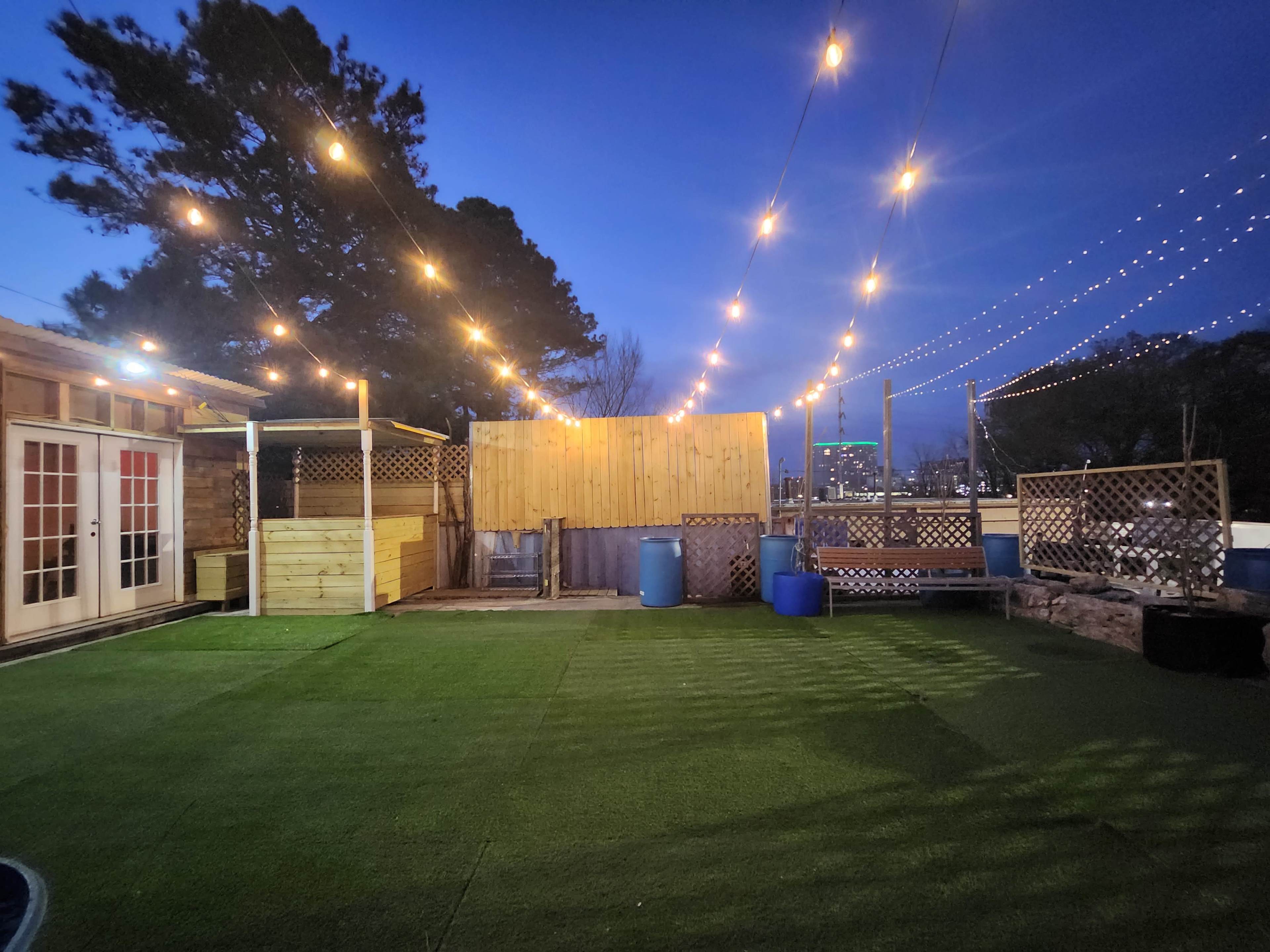 A rooftop patio area illuminated by string lights, featuring artificial grass and wooden structures.