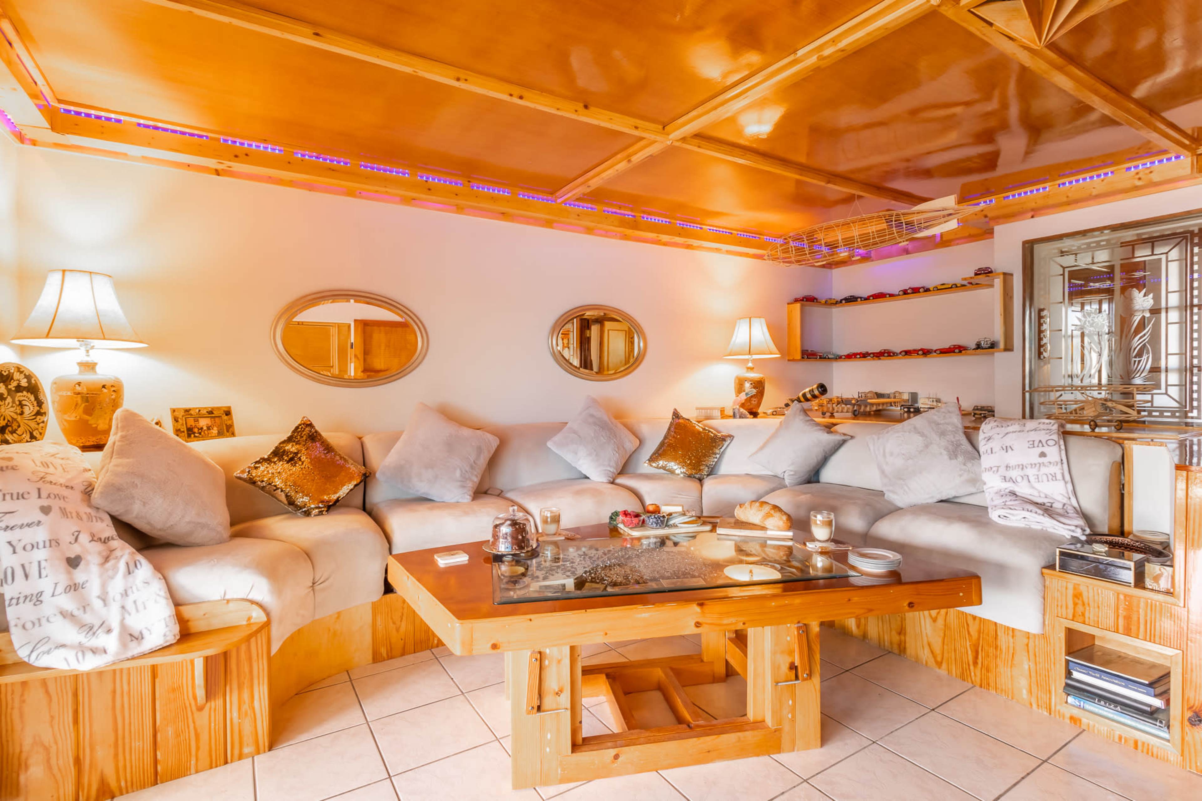 A cozy lounge area with a wooden seating arrangement, a central table, and decorative mirrors on the walls, illuminated by soft lighting.