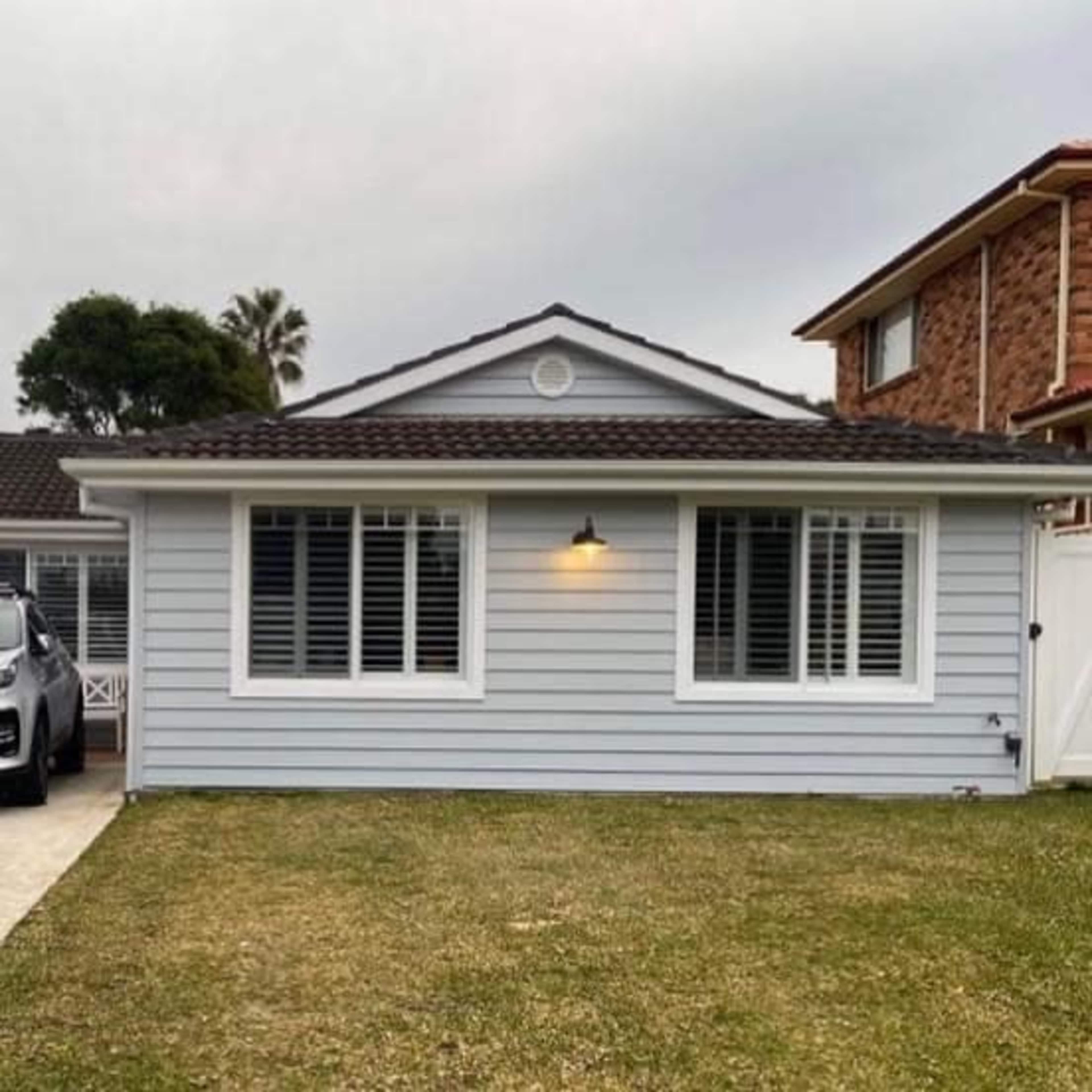 A light gray single-story house with white shutters, a small front yard, and a driveway with a parked car.