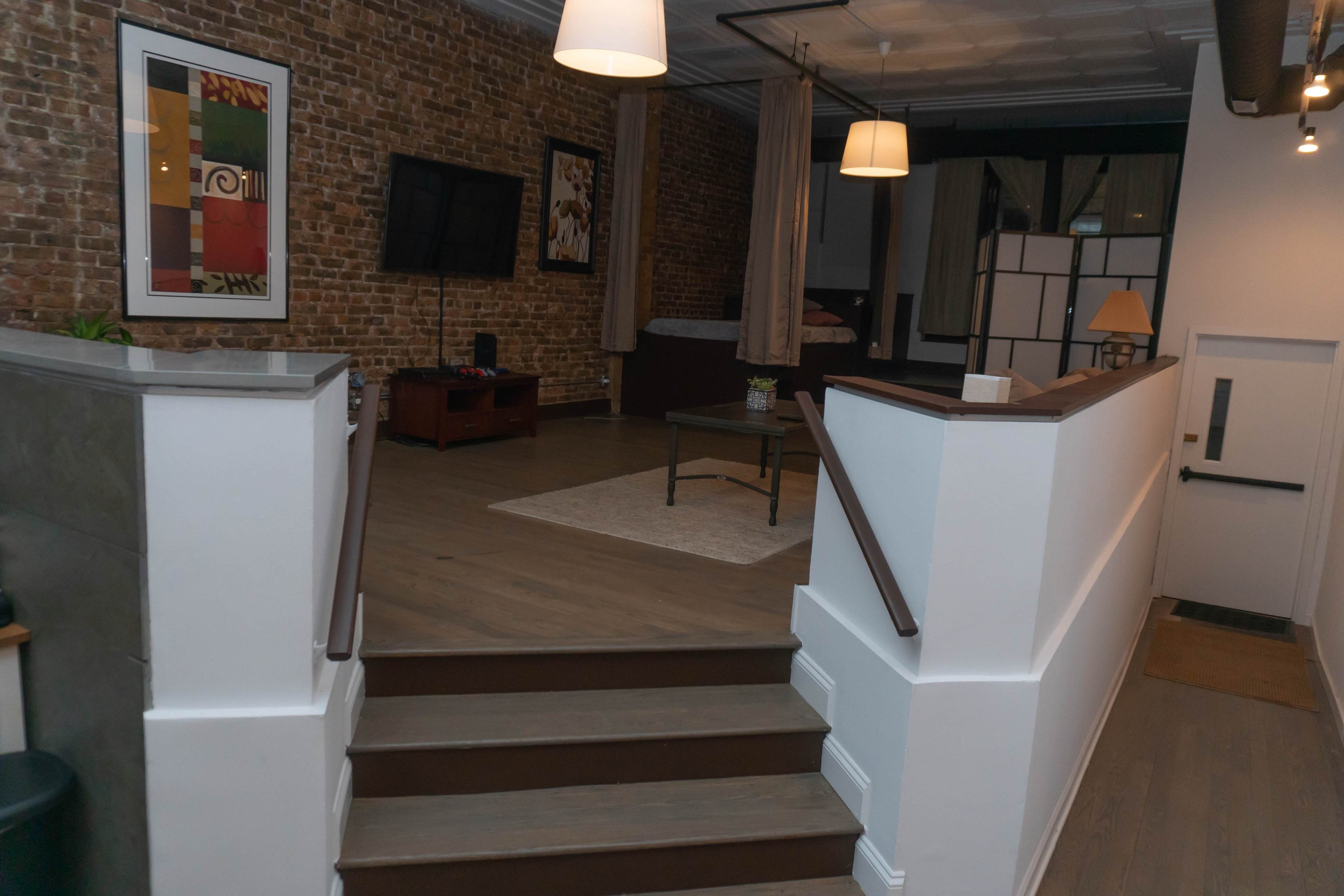 A modern interior space with a staircase leading to a room featuring exposed brick walls, a television, and a seating area.