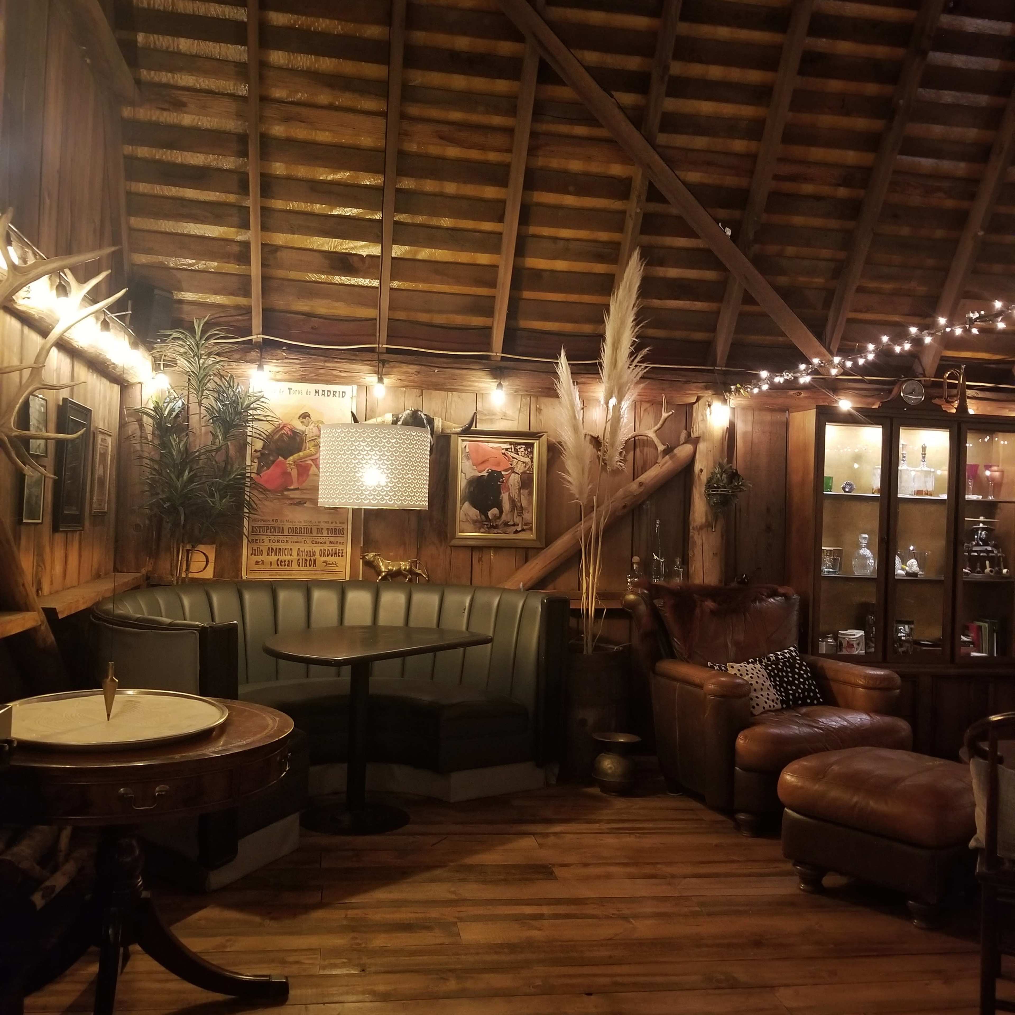 A cozy interior of a wooden cabin-style bar with a circular table, leather seating, and decorative lighting.
