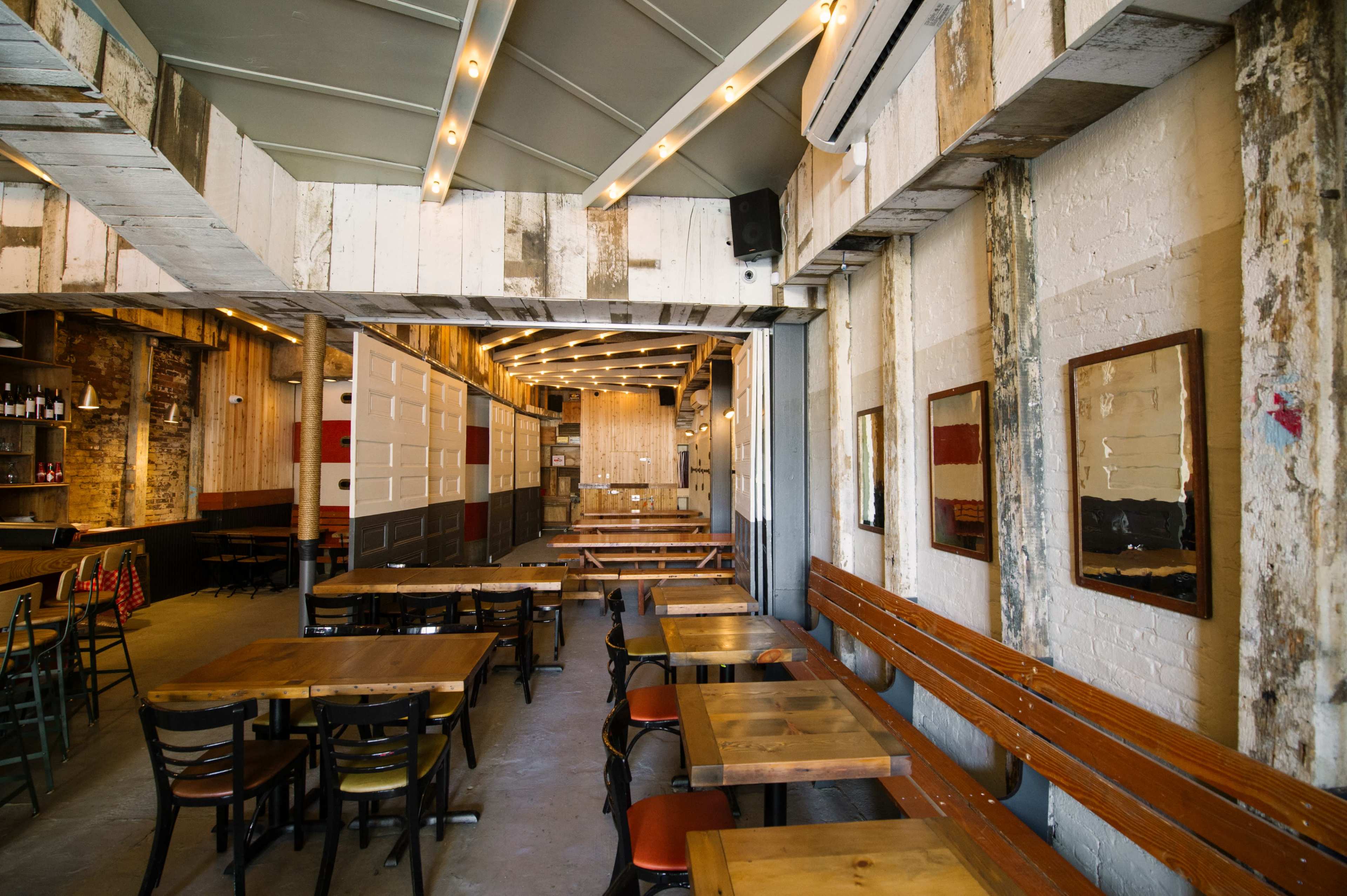 The image shows a spacious restaurant interior featuring wooden tables, chairs, and exposed brick walls, with a modern design aesthetic.
