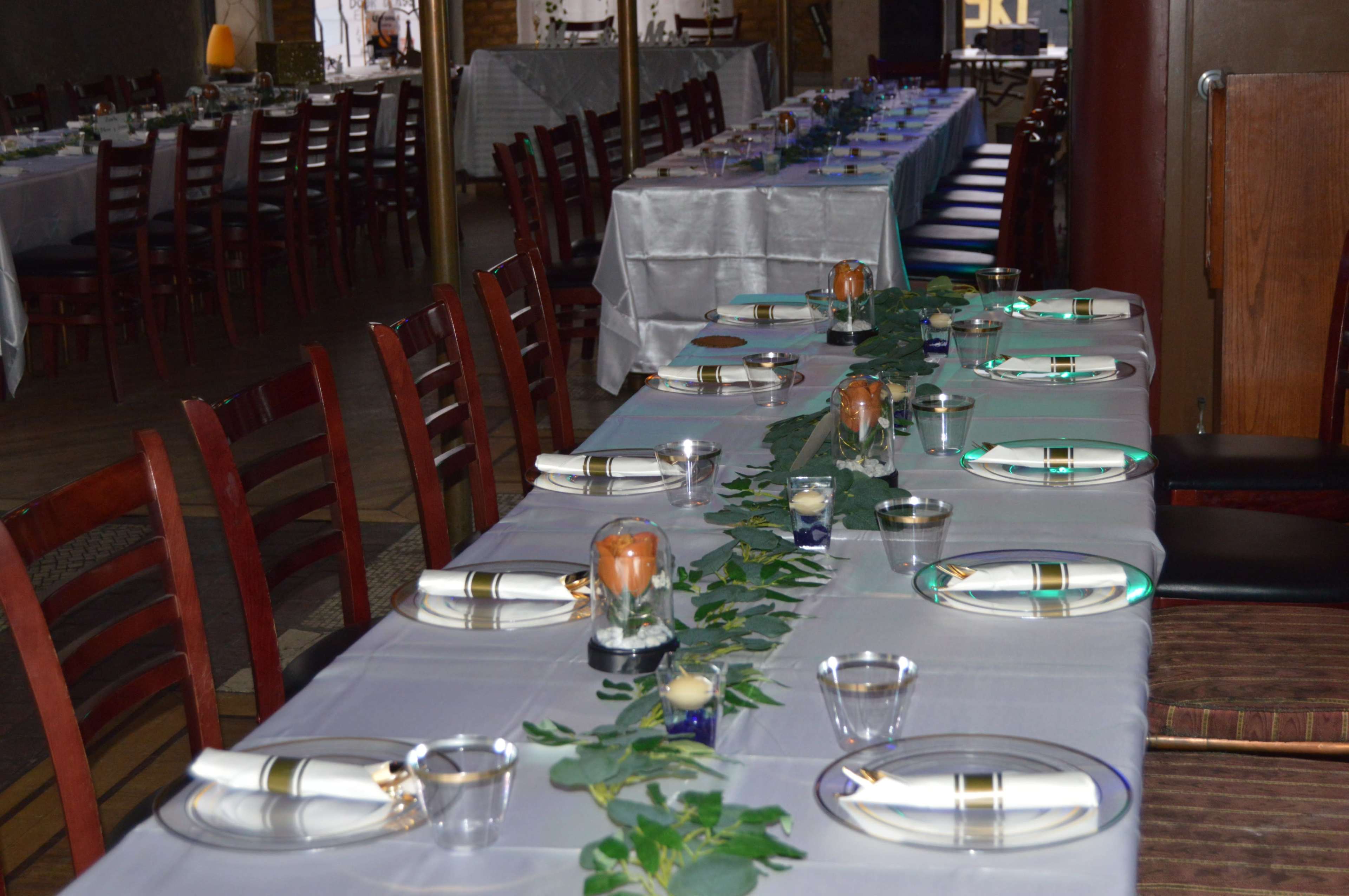 A long dining table is set with plates, utensils, and decorative elements, featuring a green floral runner and candles.