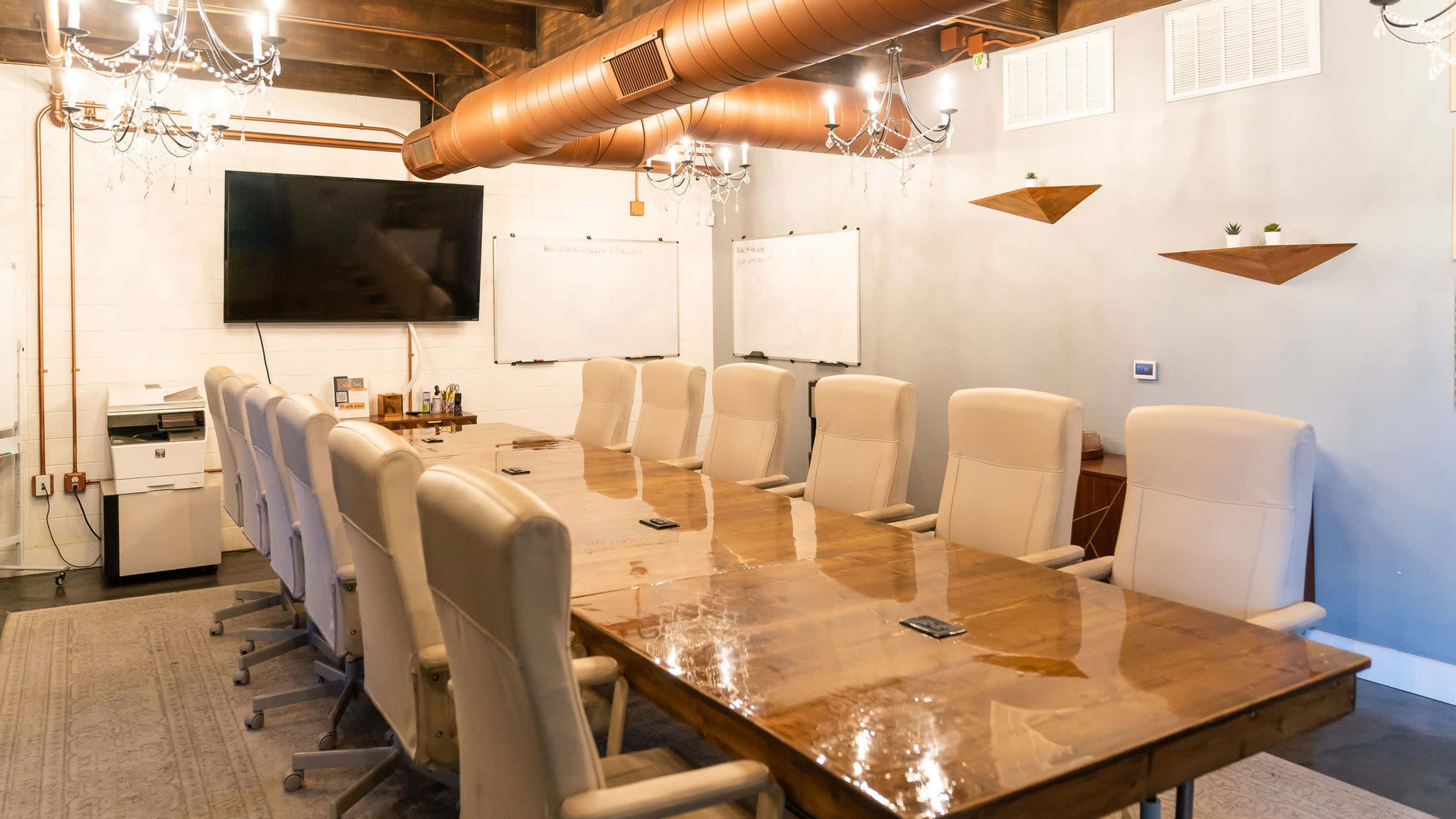 A large conference room with a long wooden table, multiple beige chairs, and a wall-mounted television.