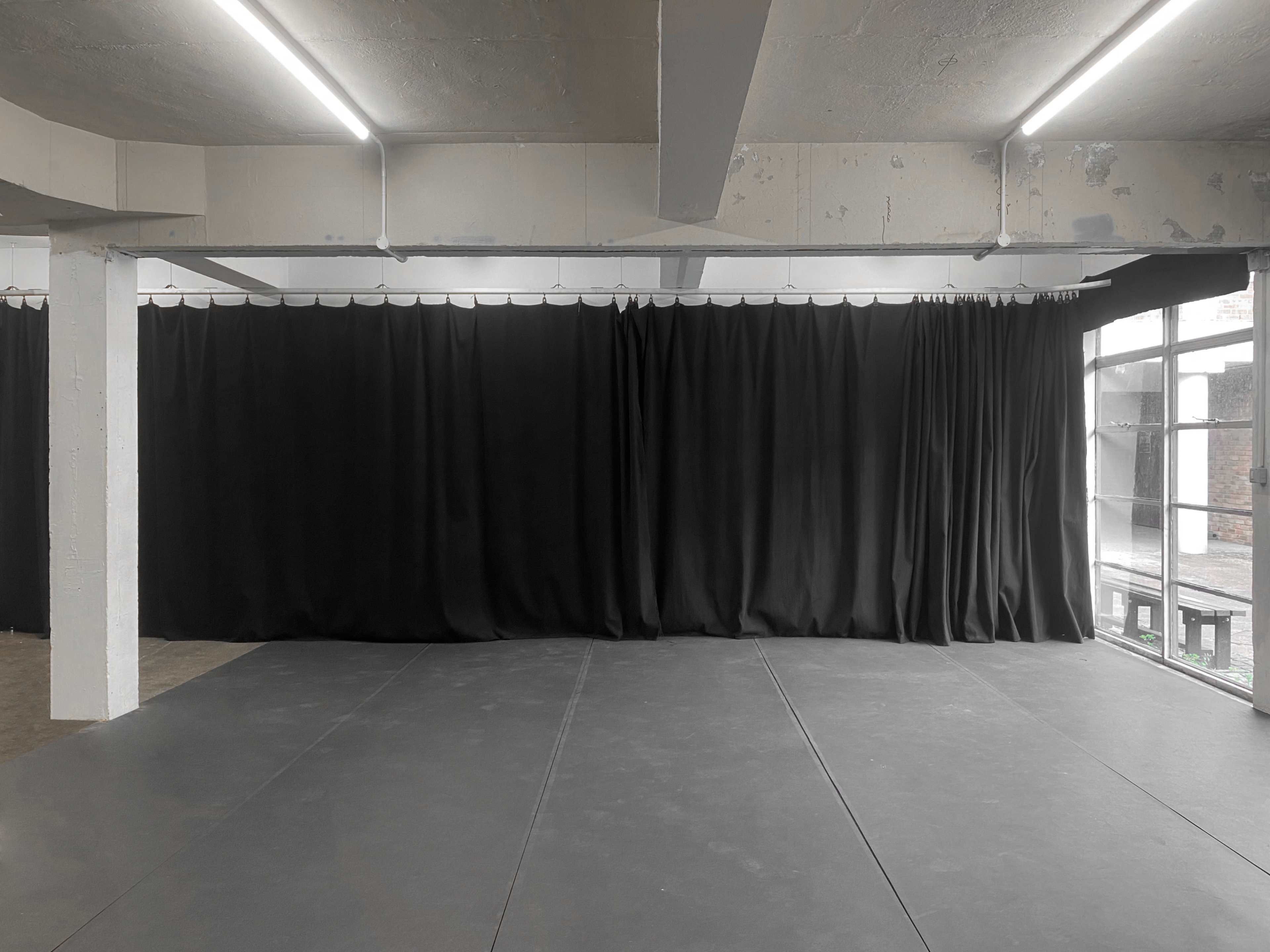 A spacious room with a dark floor and black curtains along one wall, illuminated by overhead lights.