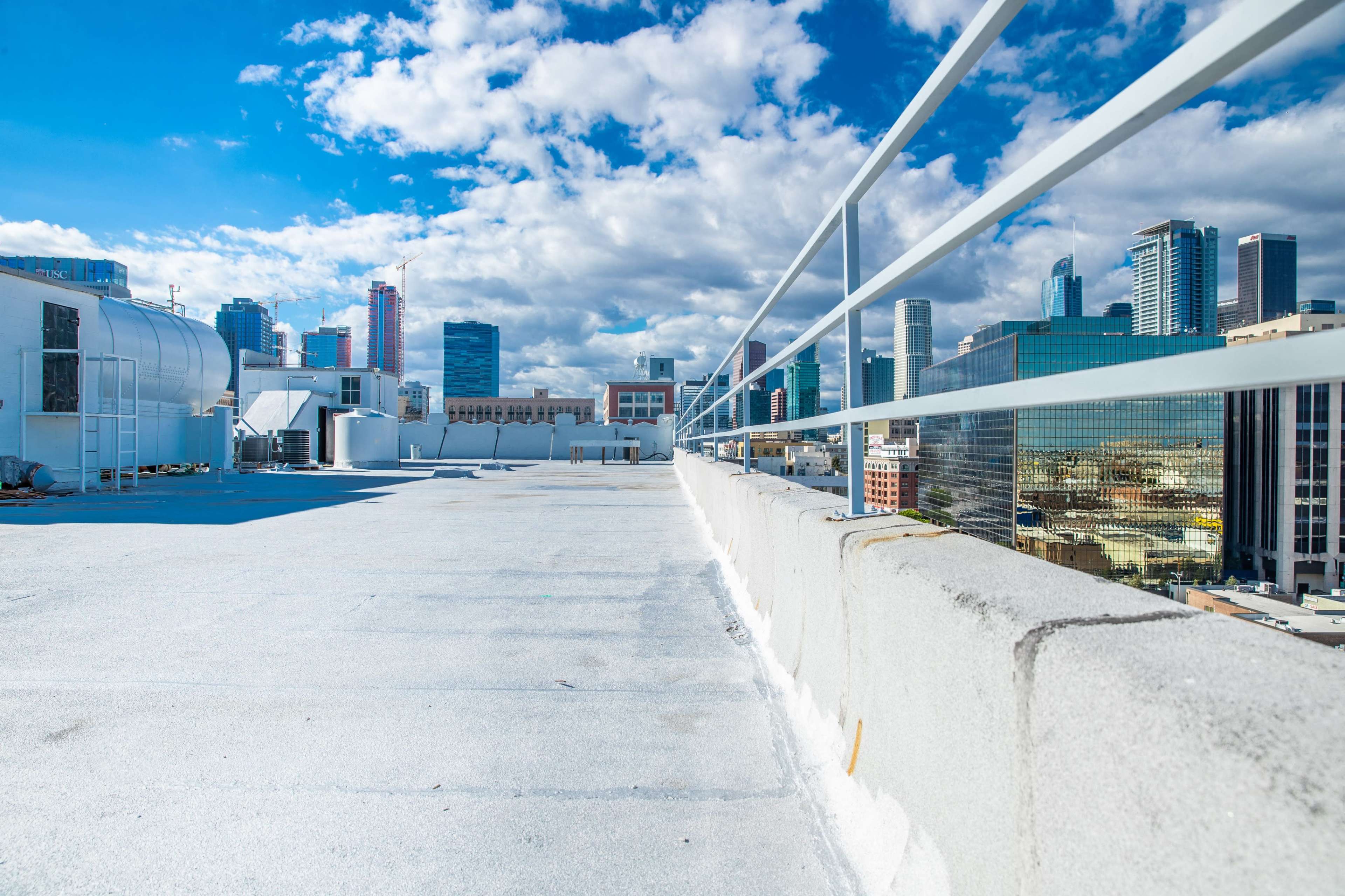The image shows a rooftop view of a city skyline with tall buildings under a partly cloudy sky.