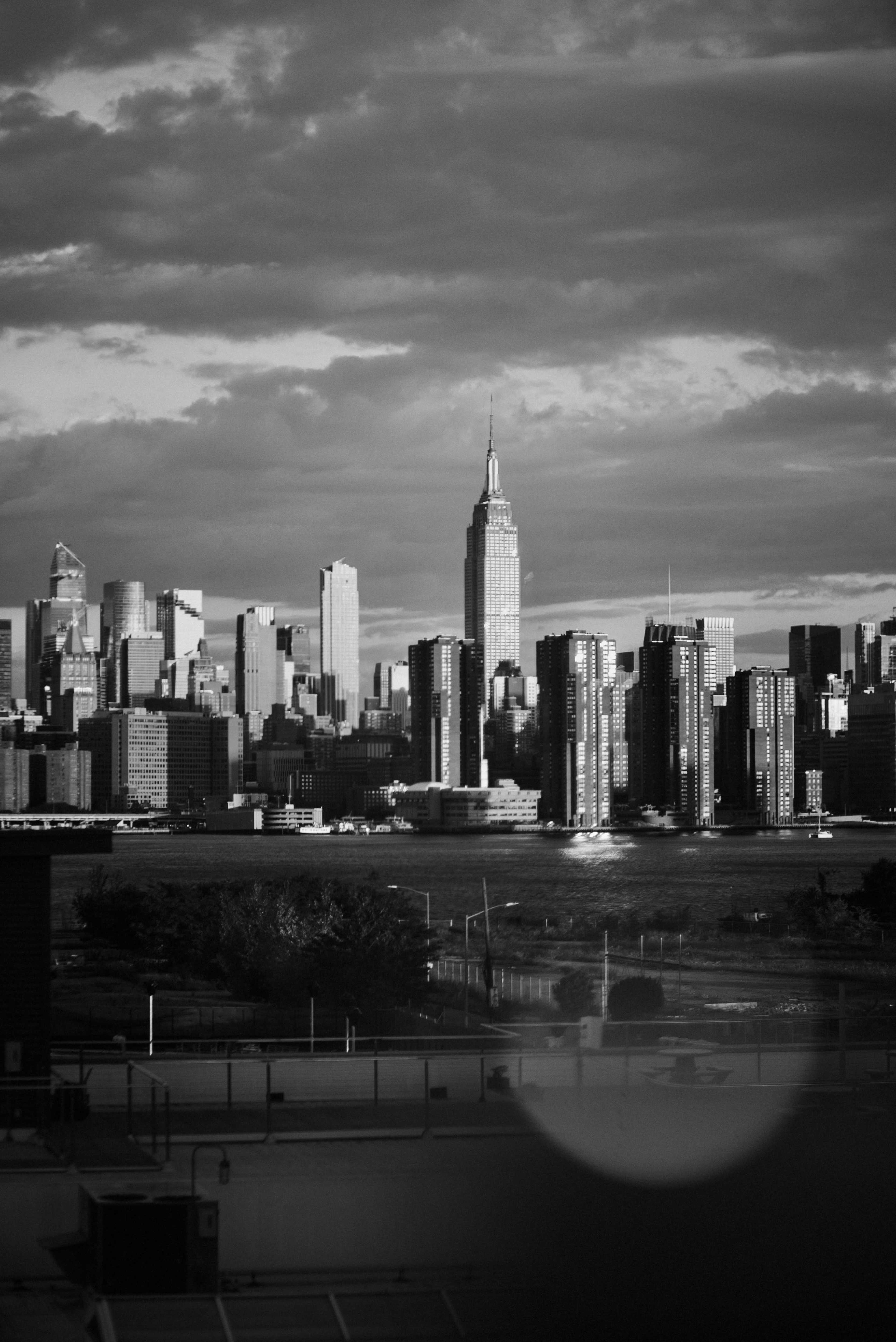 A black and white cityscape features the Empire State Building prominently among tall buildings against a cloudy sky.