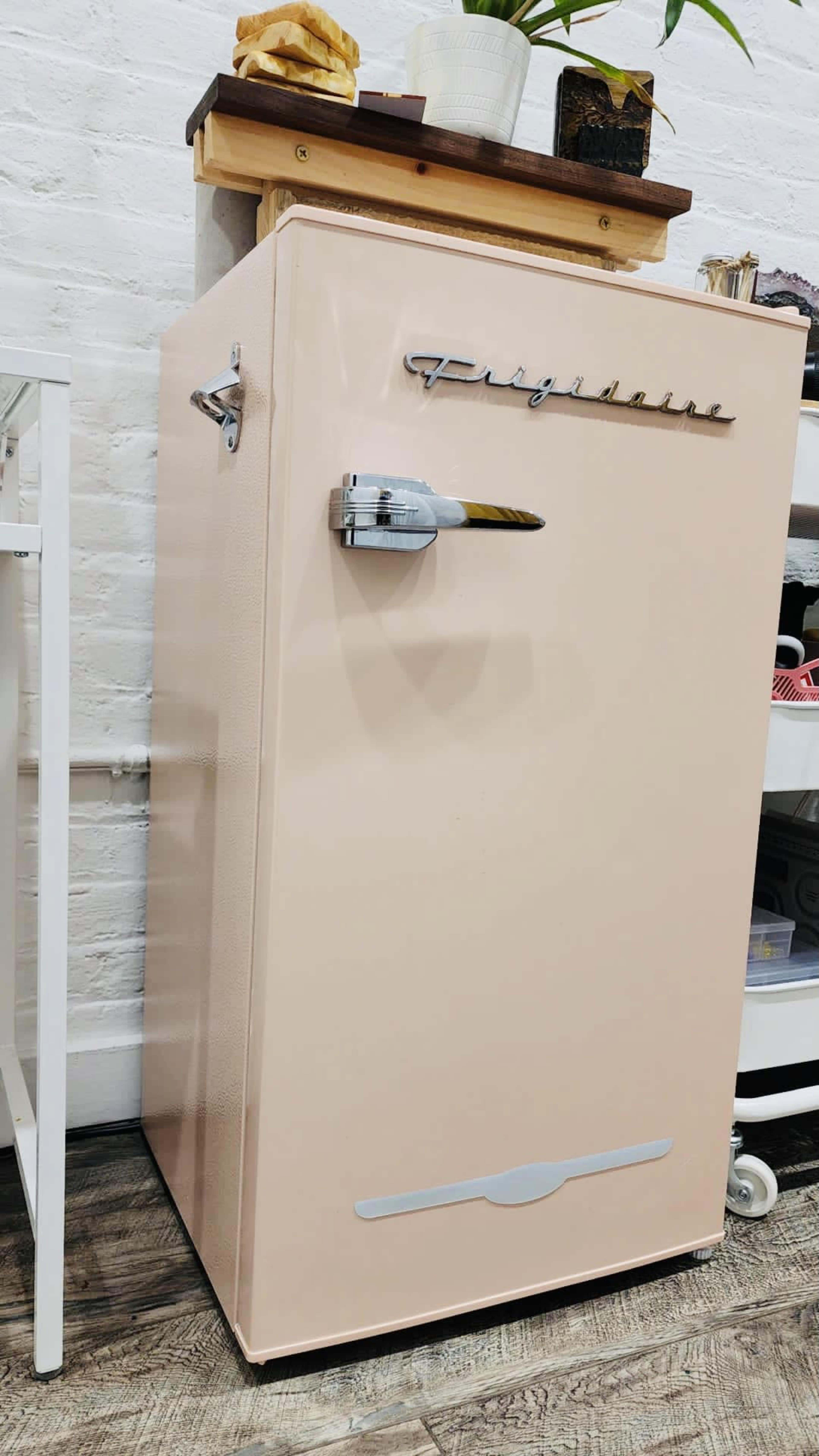 A vintage pink Frigidaire refrigerator positioned against a white brick wall.
