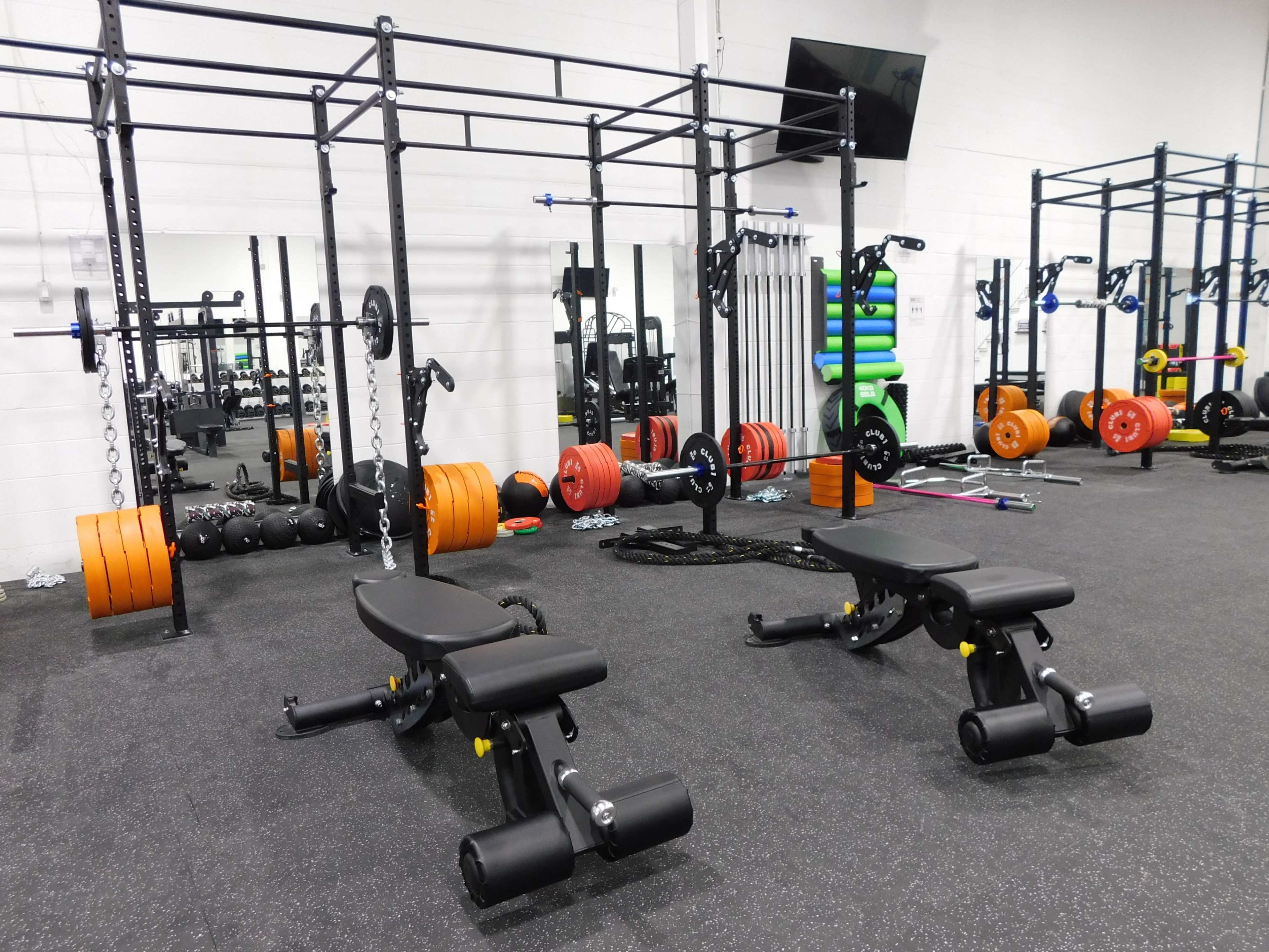 A modern gym with weight benches, various weights, and strength training equipment arranged across the room.