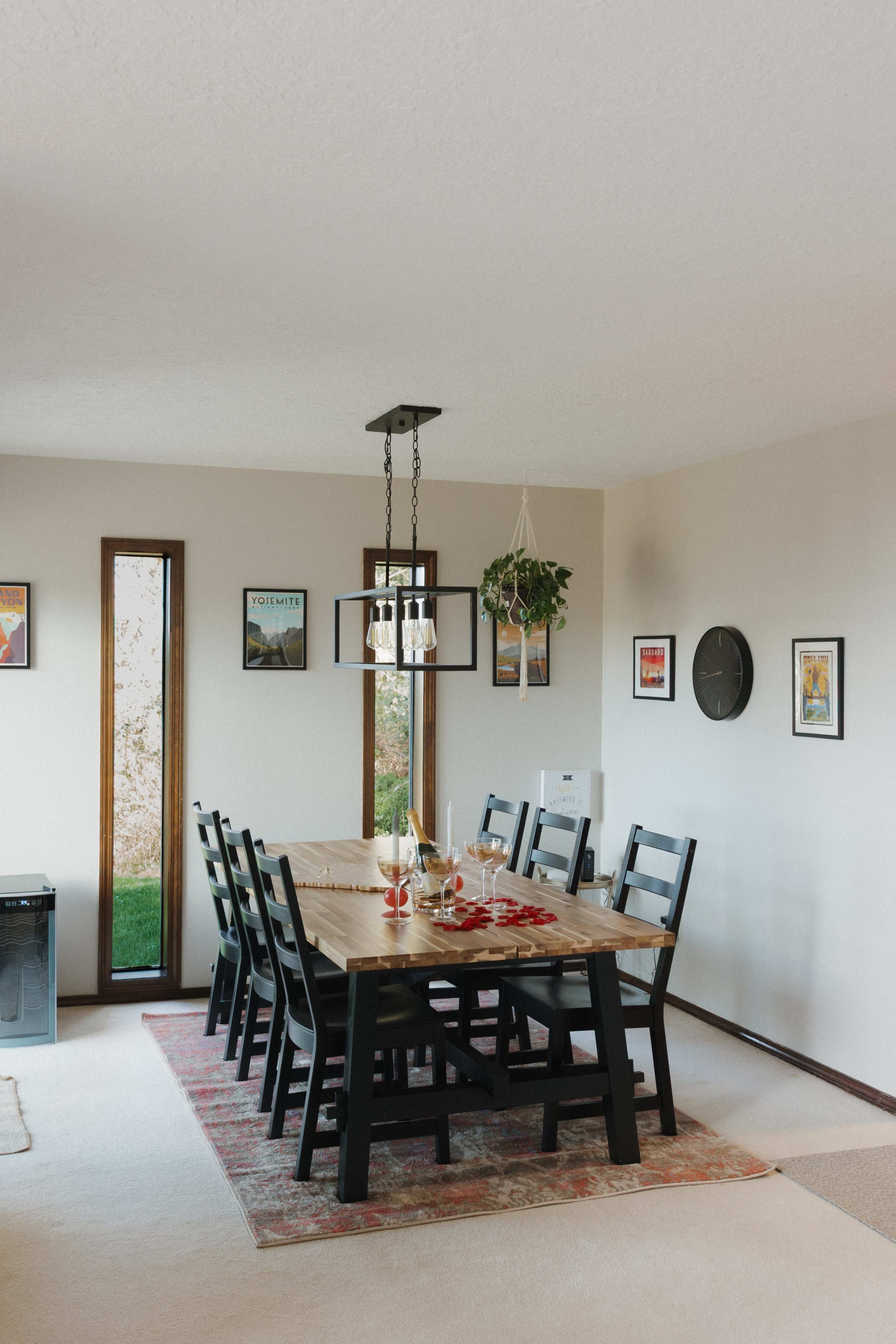 A spacious dining room features a long wooden table surrounded by black chairs, with artwork on the walls and a window providing natural light.