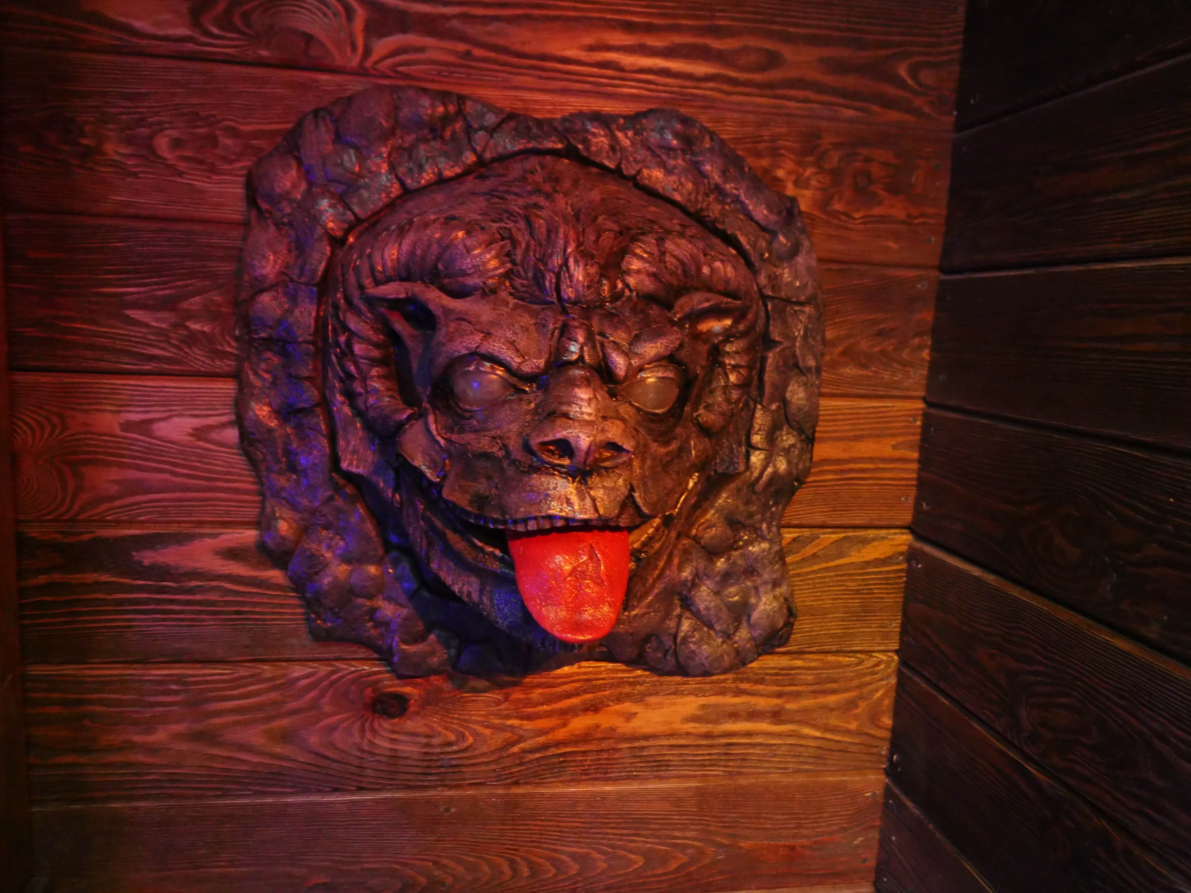 A textured sculpture of a dog's head with a protruding tongue is mounted on a wooden wall.