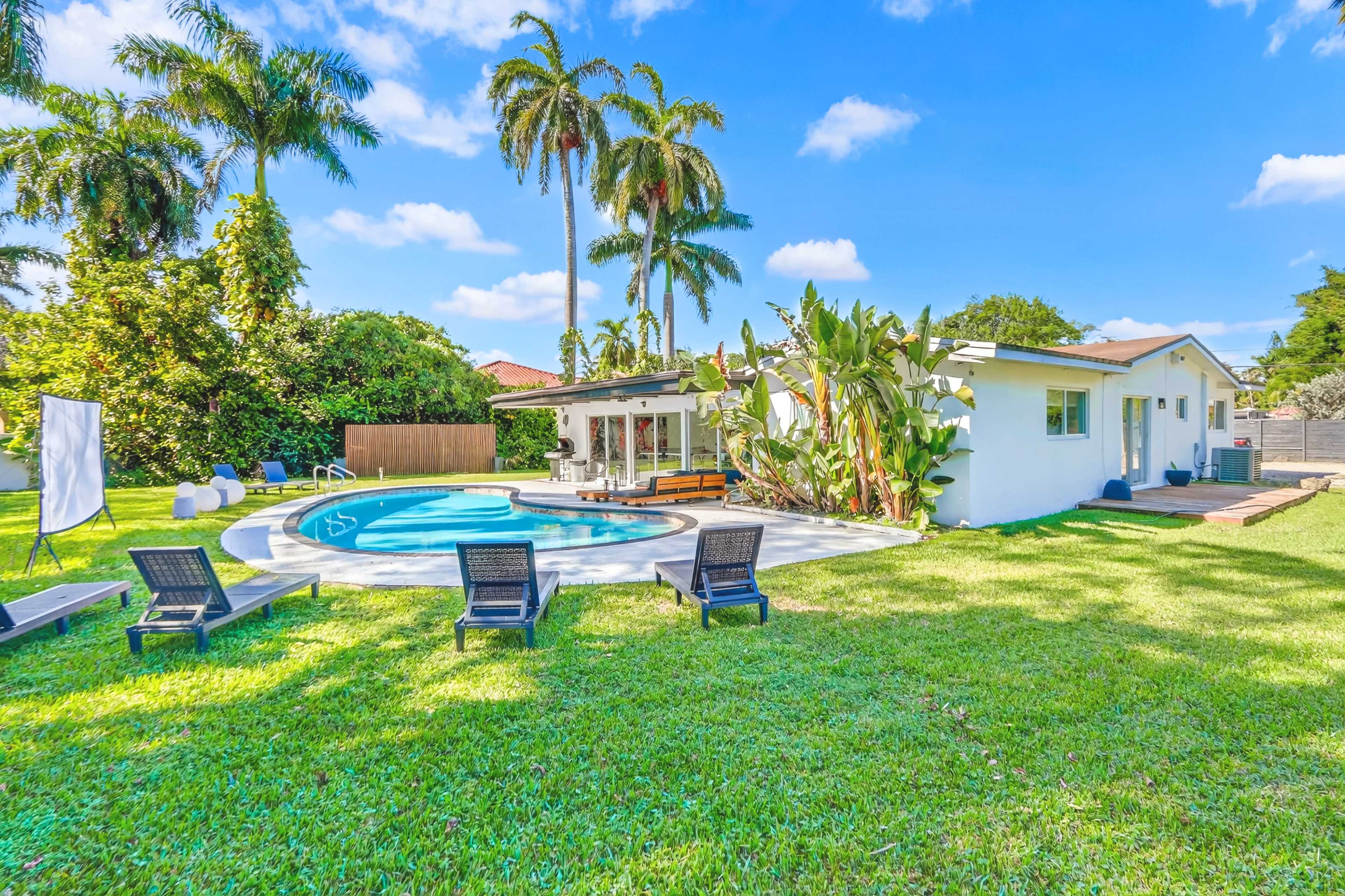 The image shows a backyard with a swimming pool, lounge chairs, palm trees, and a house surrounded by green grass.