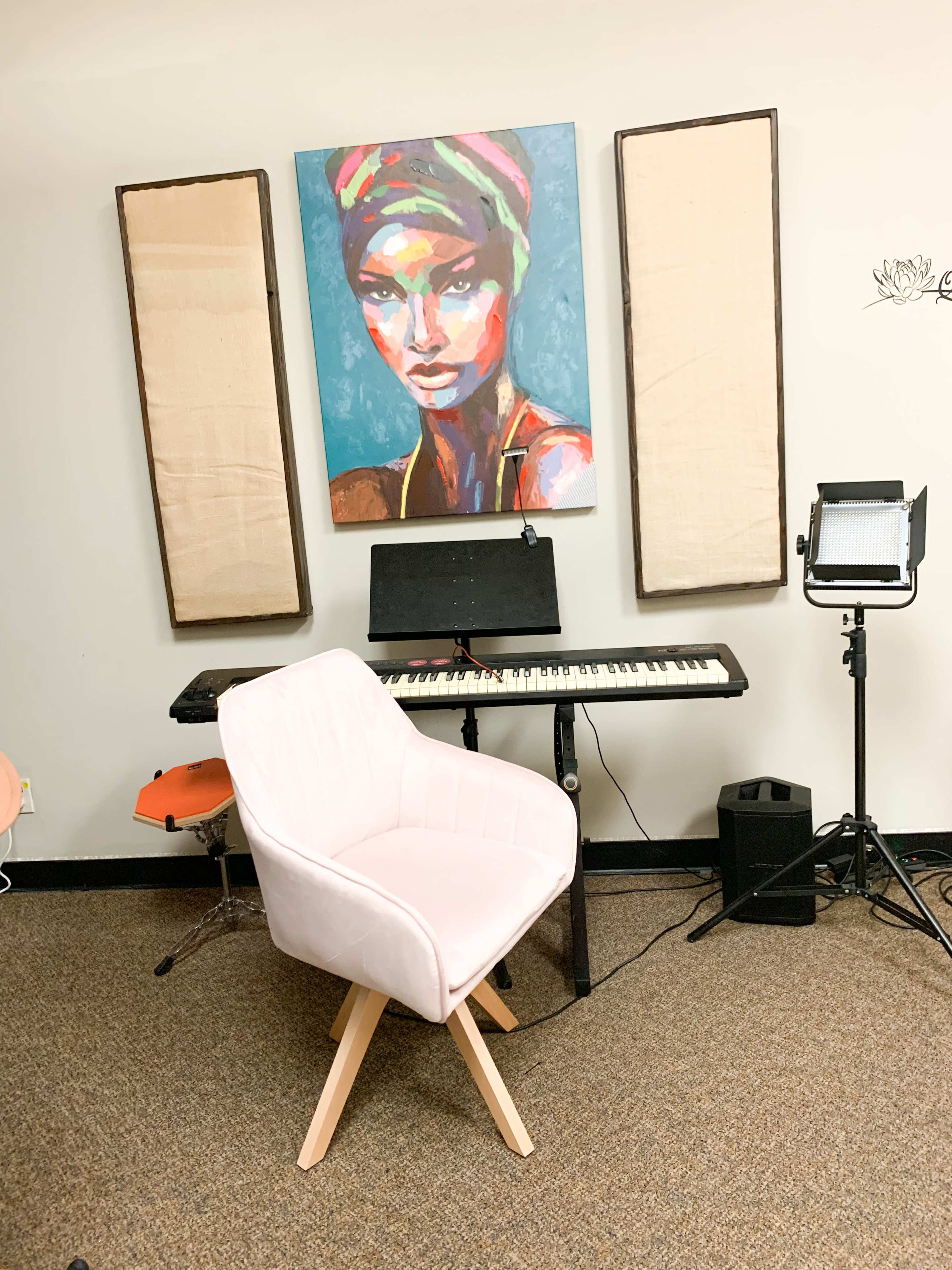 A pink chair sits in front of a keyboard and a colorful portrait of a woman, surrounded by two large panels on the wall.