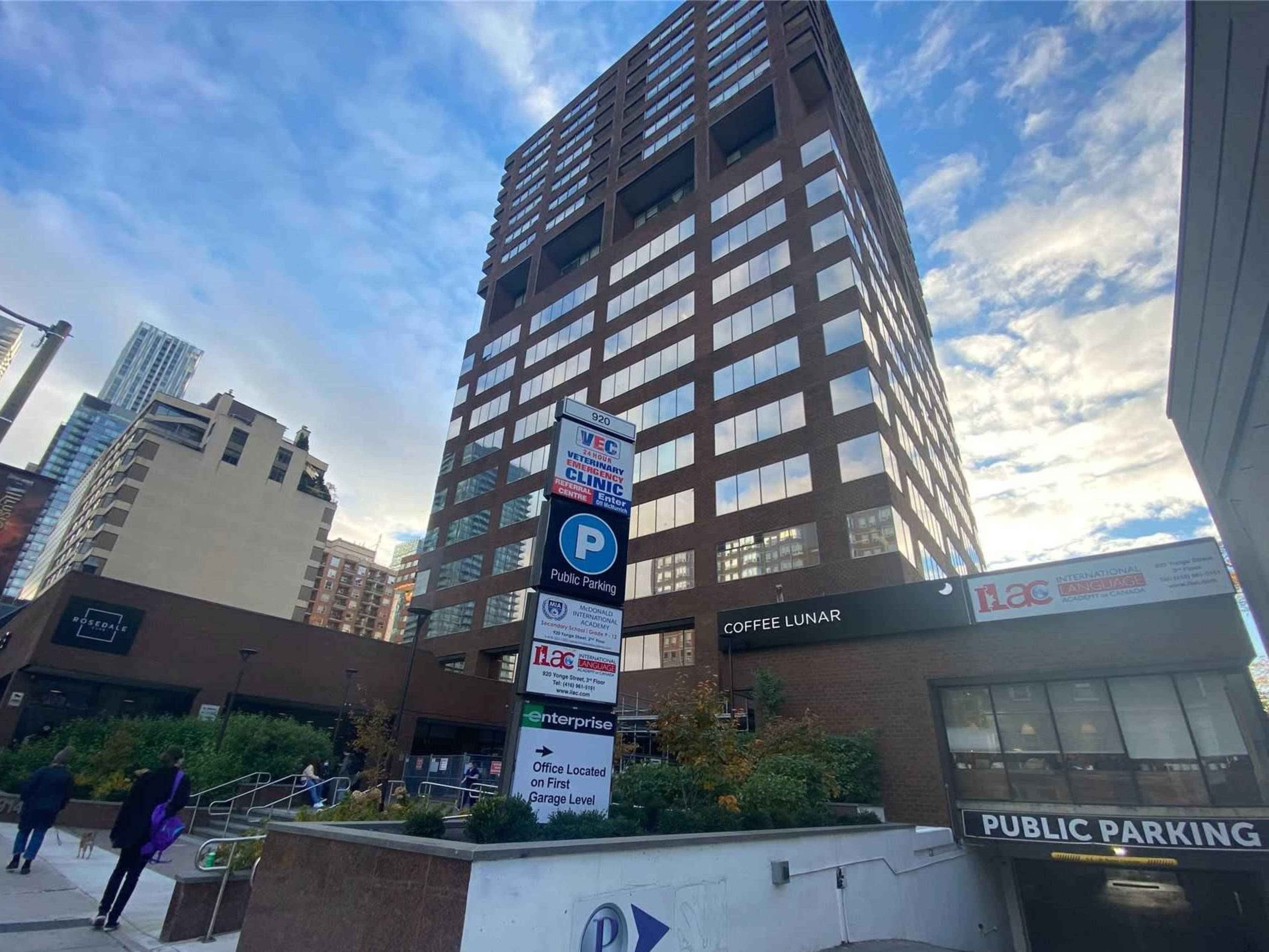 A large brown office building with a sign for "Coffee Lunar" and public parking is located in an urban area with cloudy skies.