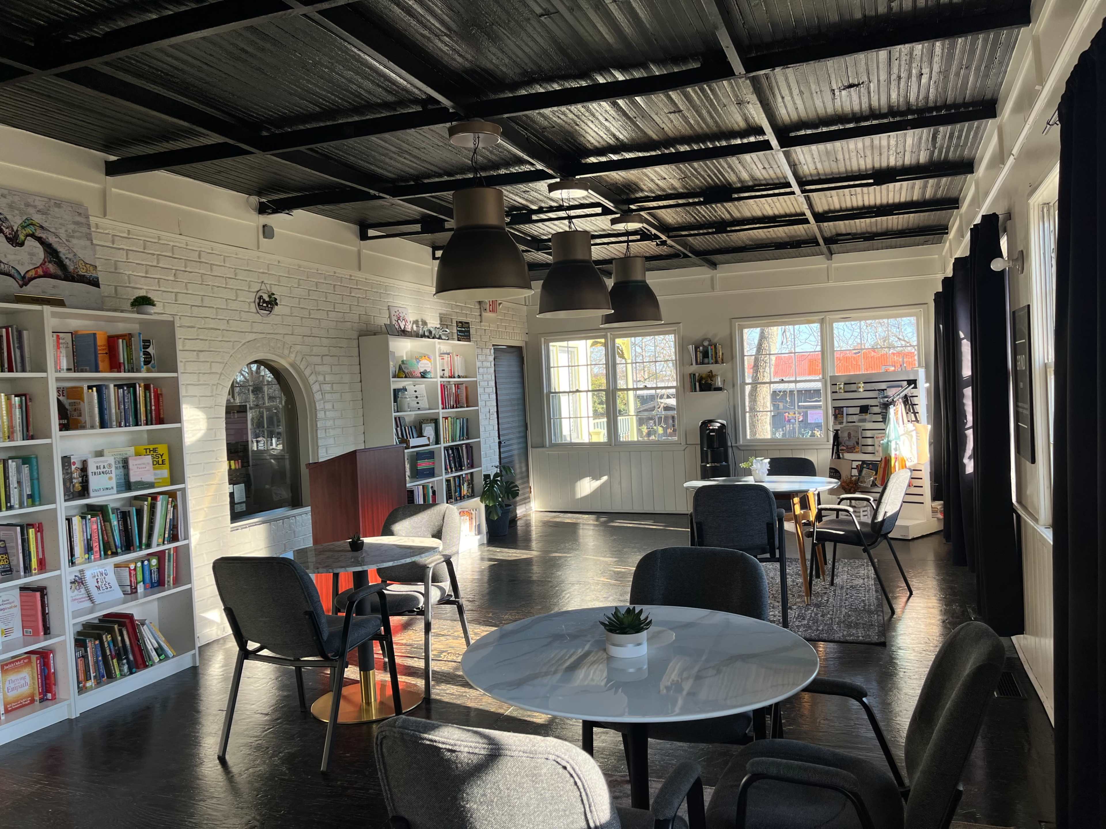A bright, modern library or reading space with shelves of books, circular tables, and large windows.