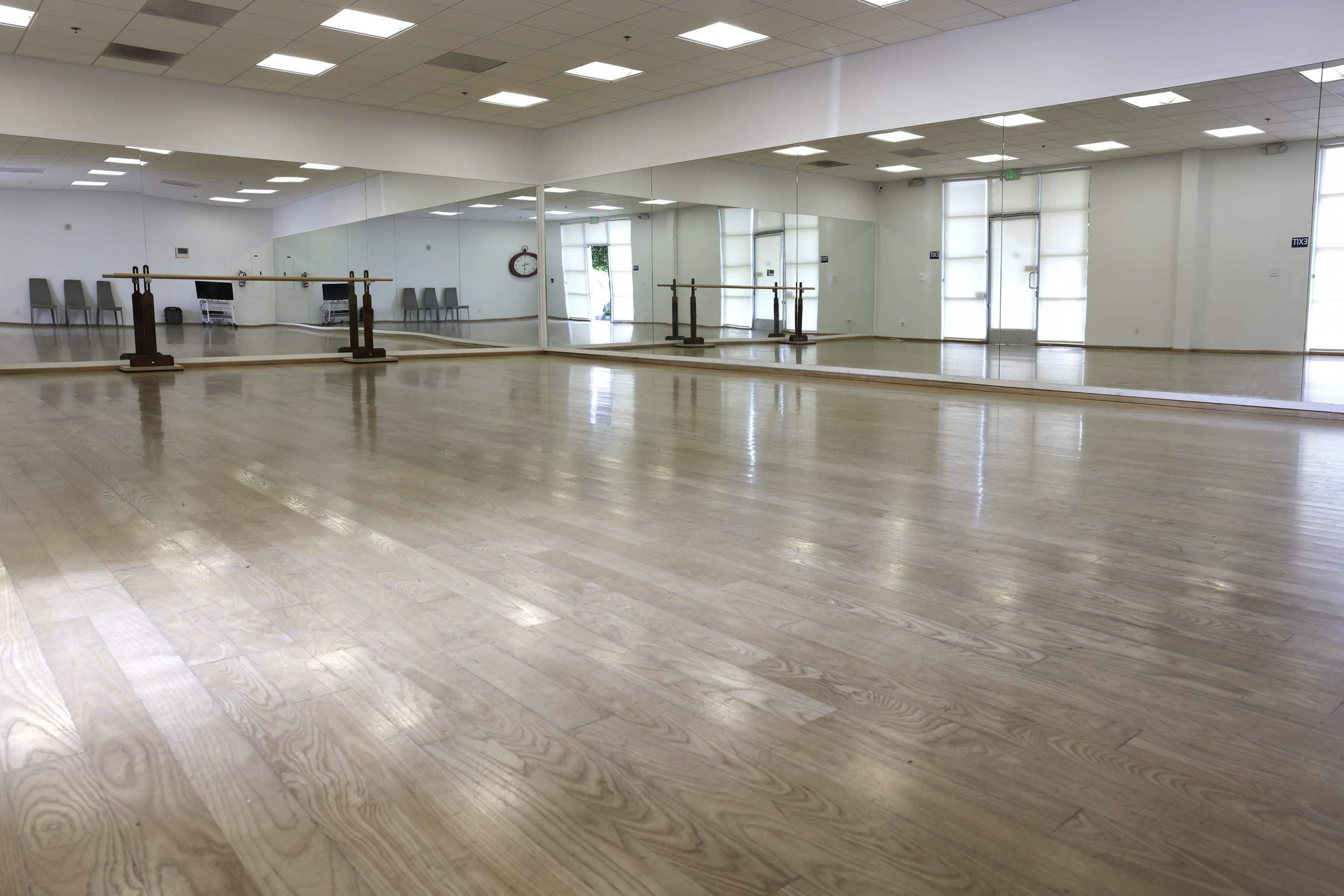 A spacious dance studio with polished wooden floors and large mirrors along one wall.