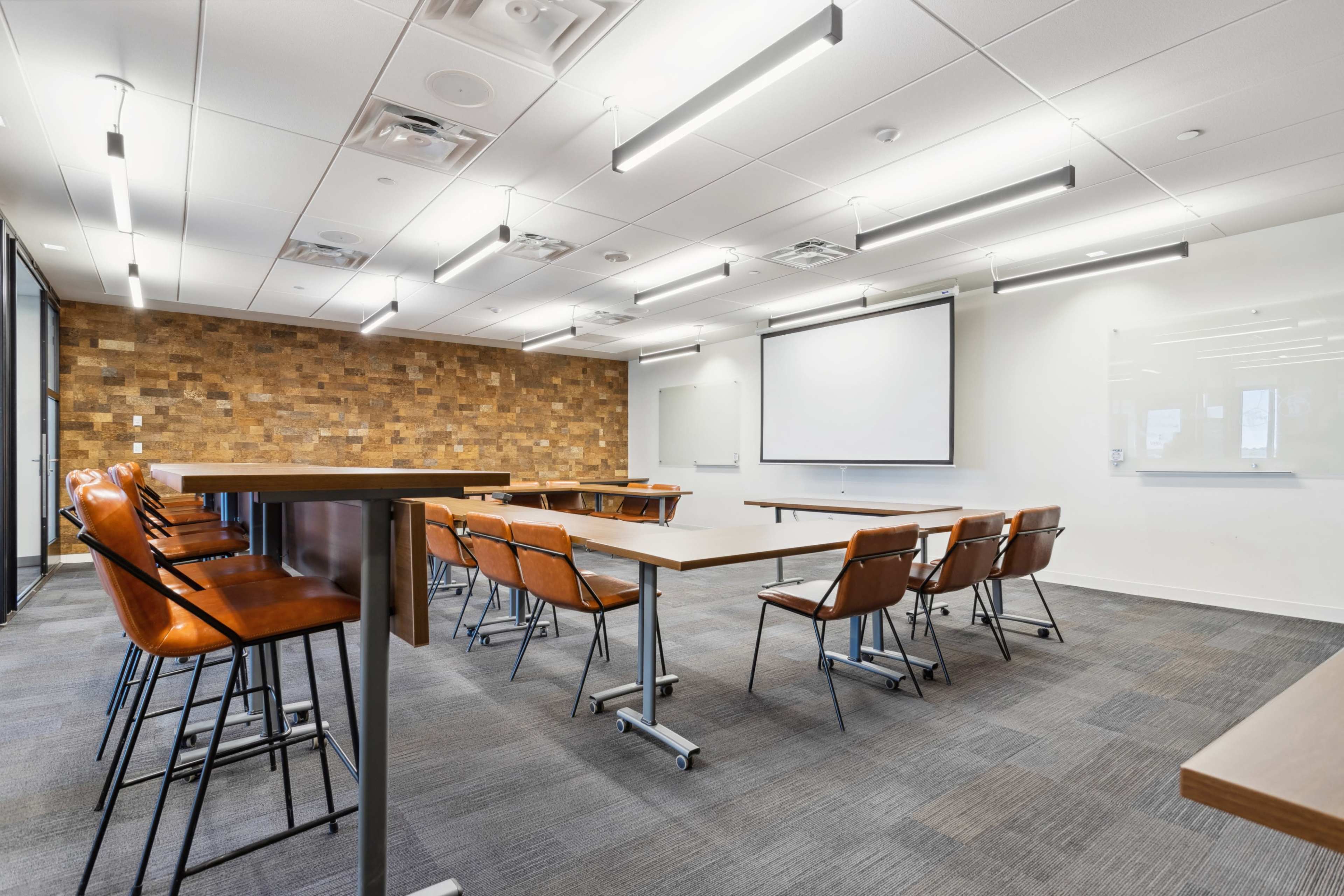 The image shows a modern conference room with wooden accent walls, several tables, and chairs arranged for a meeting.