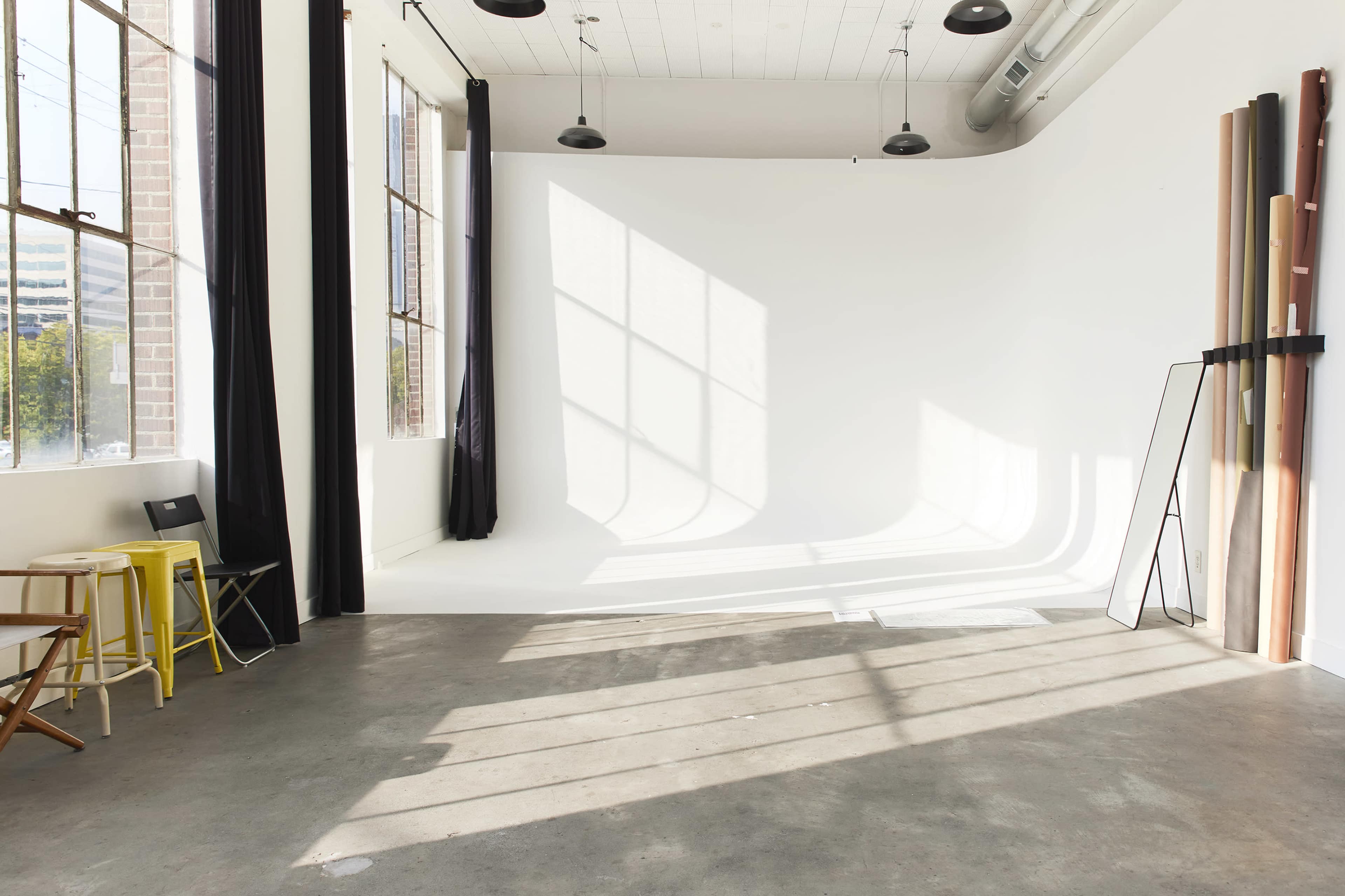 The image shows a spacious photo studio with large windows, a white backdrop, and various items arranged along one wall.