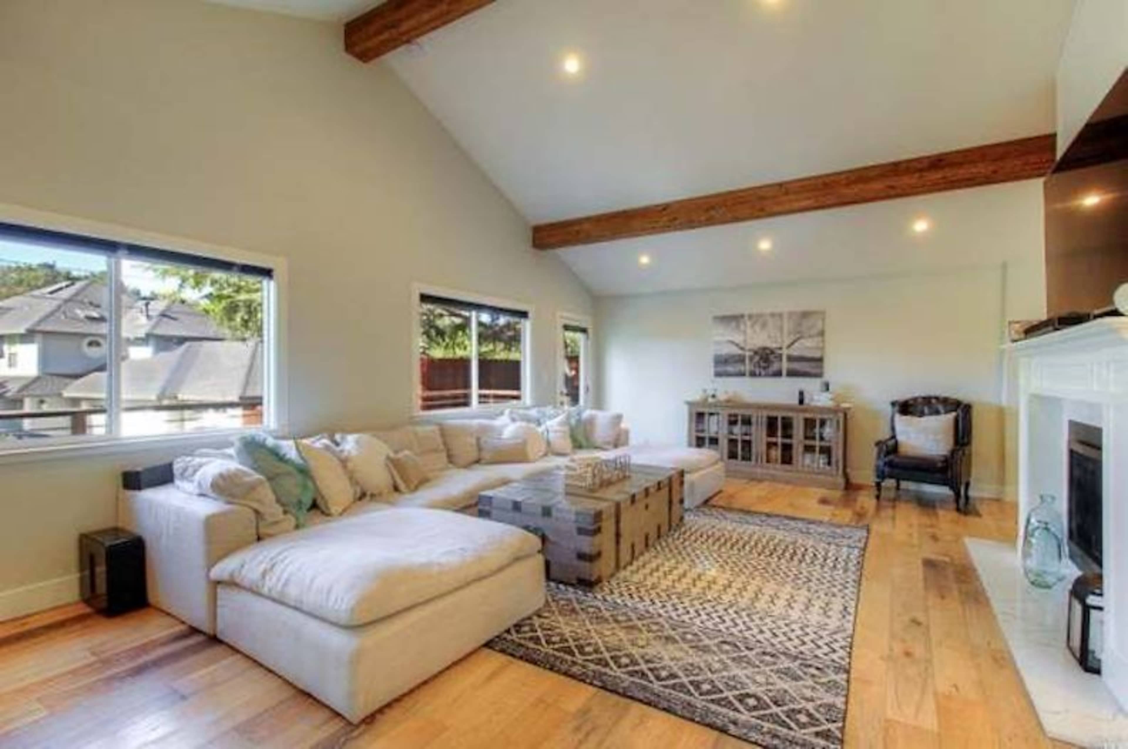 The living room features a large sectional sofa, a coffee table, and a decorative rug under a vaulted ceiling with exposed wooden beams.