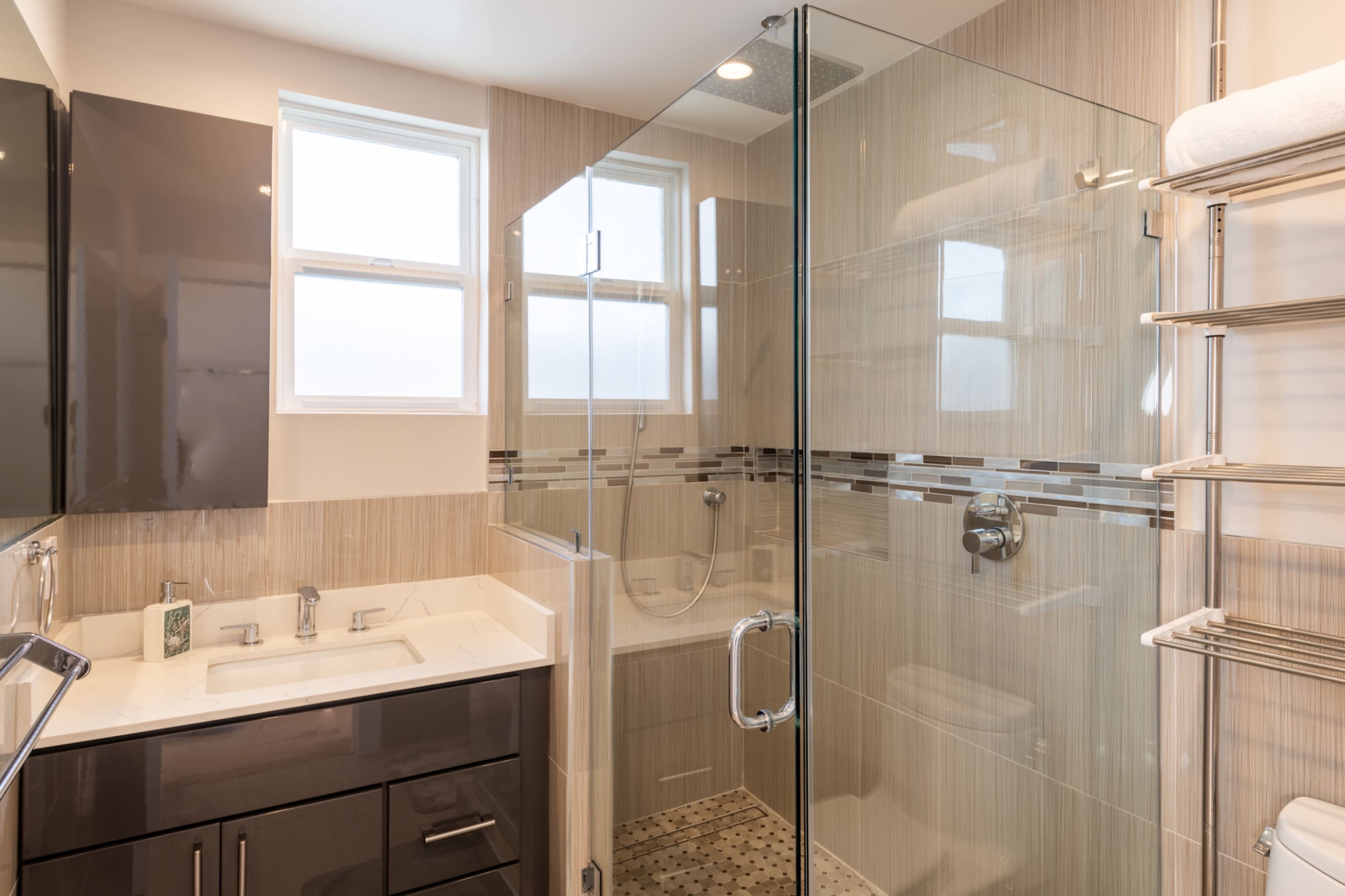 The image shows a modern bathroom featuring a glass shower enclosure, a double sink vanity, and tiled walls.