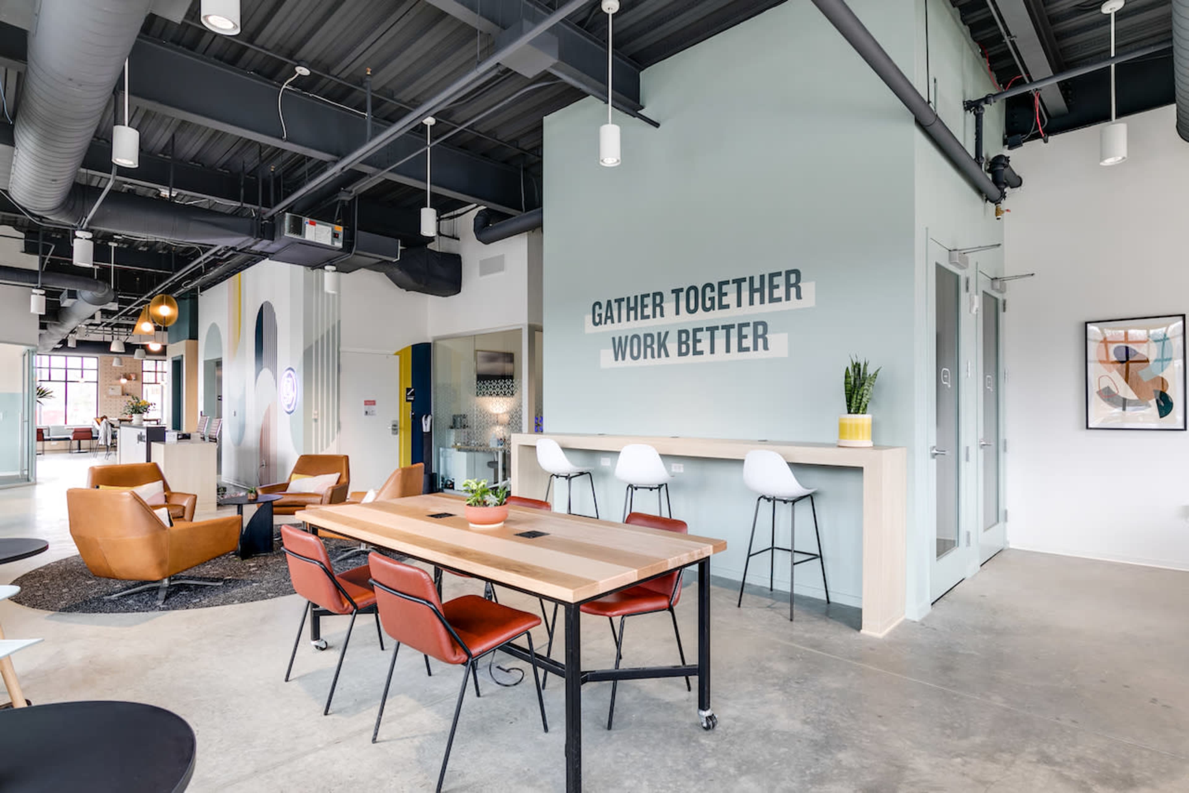 A modern workspace with a dining table, seating area, and motivational text on the wall.