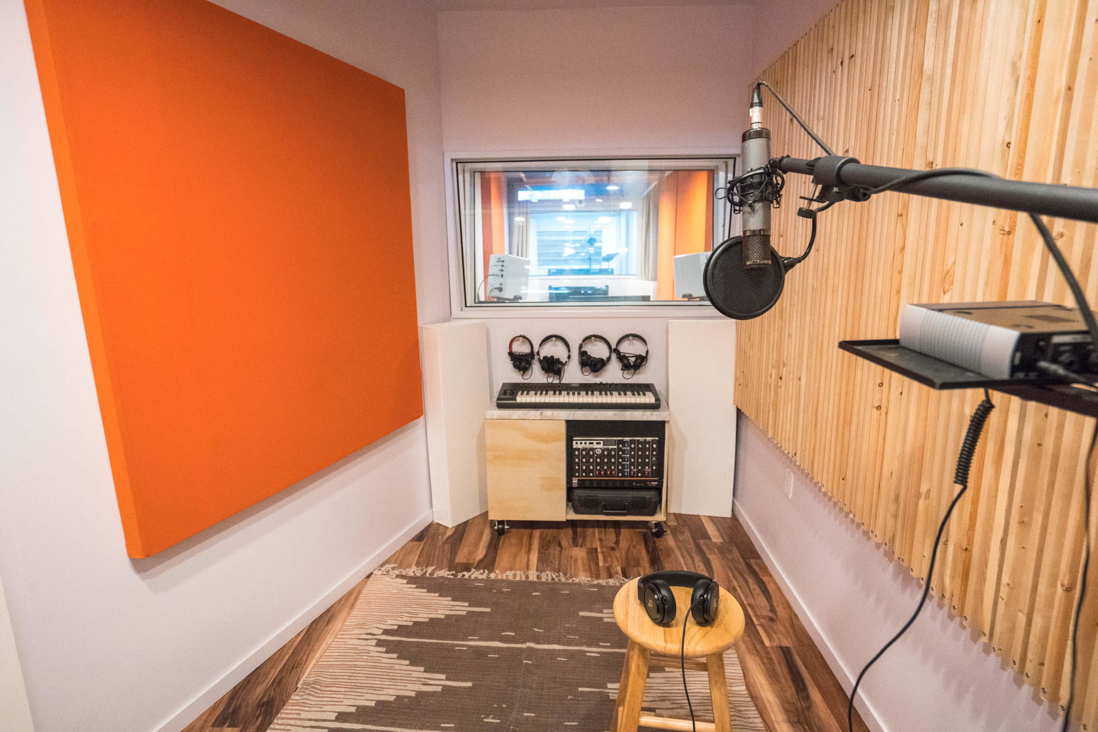 A recording studio with a microphone, headphones, and soundproofing panels on the walls, along with a wooden stool and a digital audio workstation.