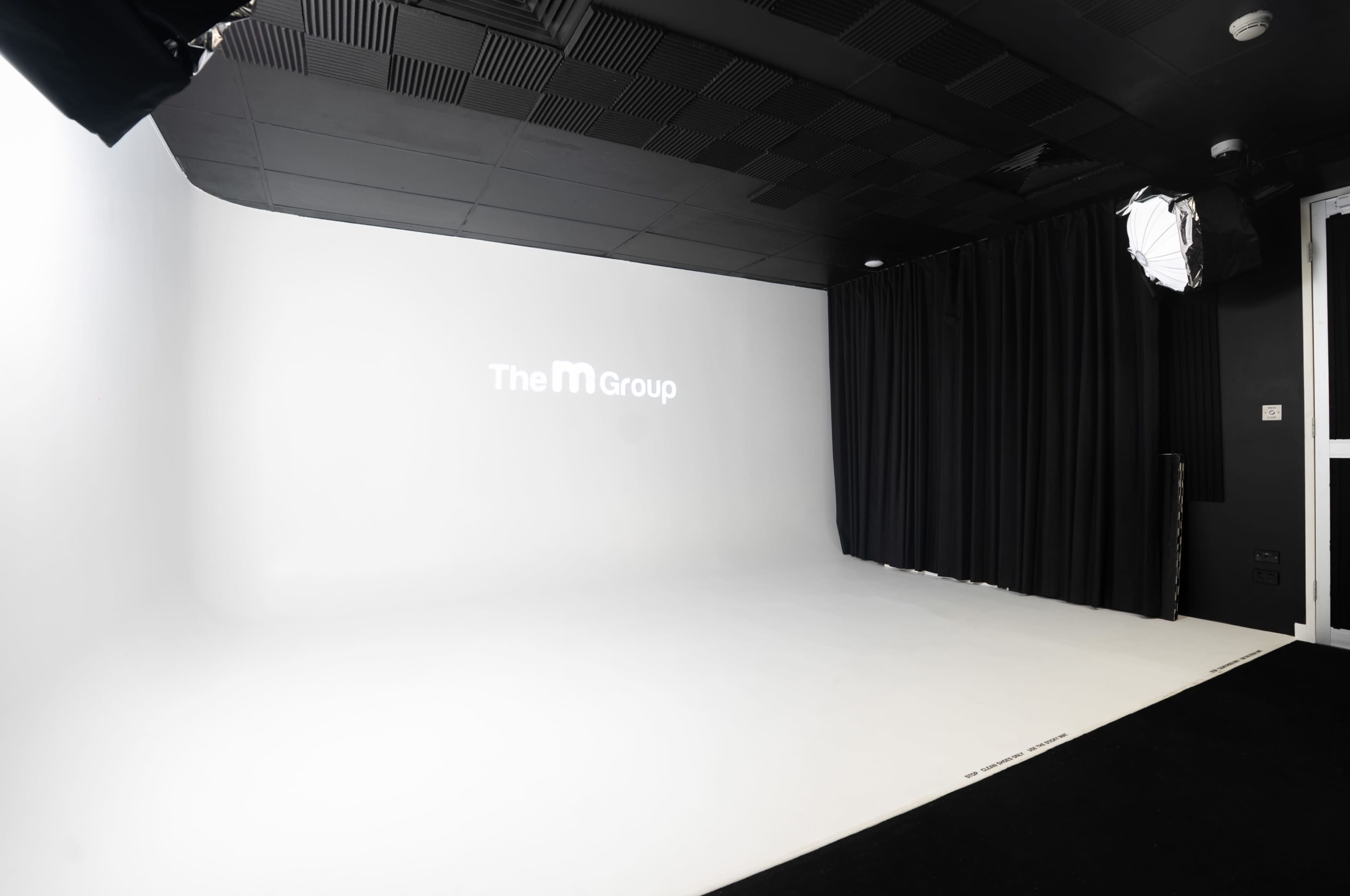 The image shows a spacious photography studio with a white backdrop and soft black curtains on one side.