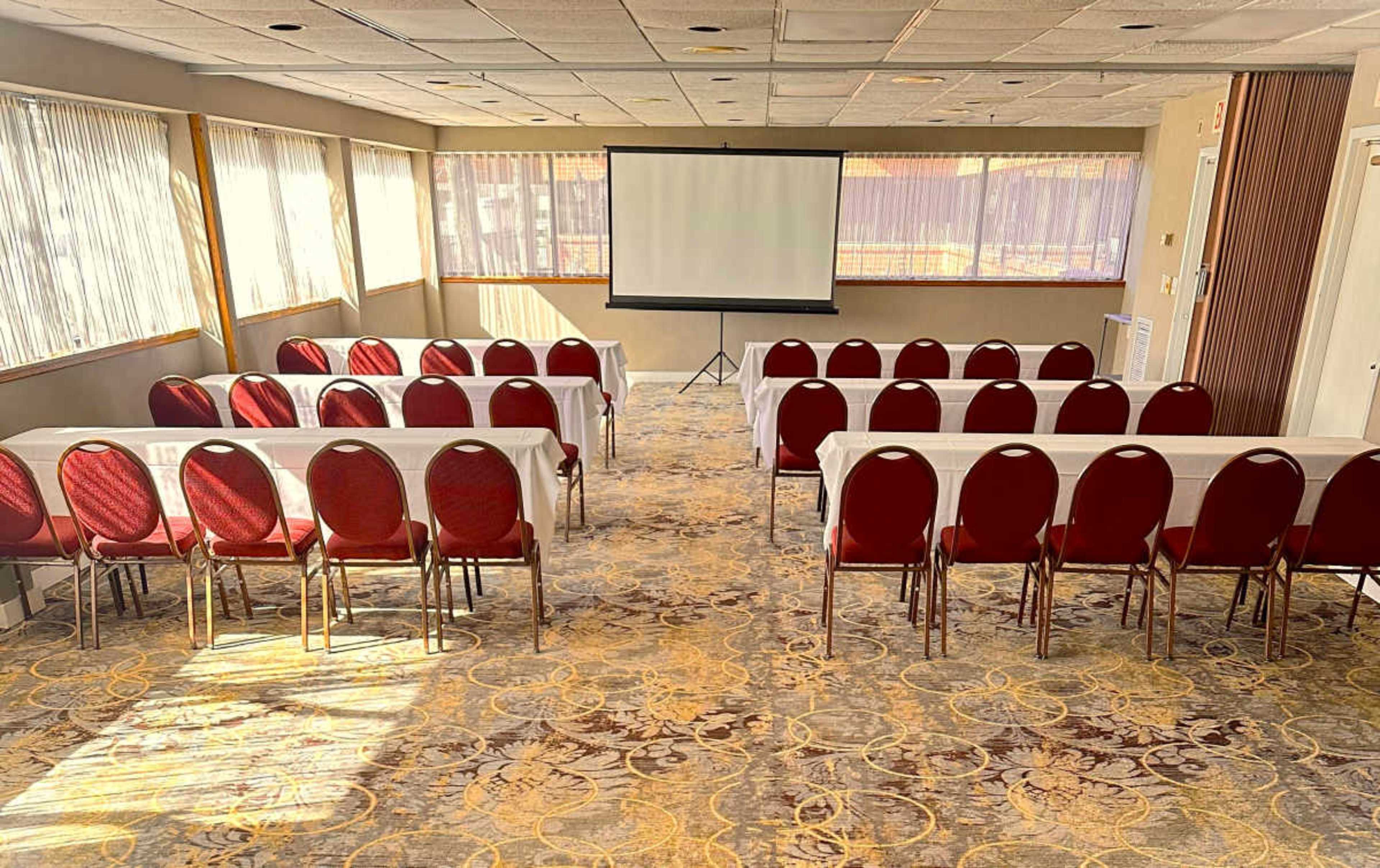 A conference room with rows of red chairs and white tables facing a projection screen.