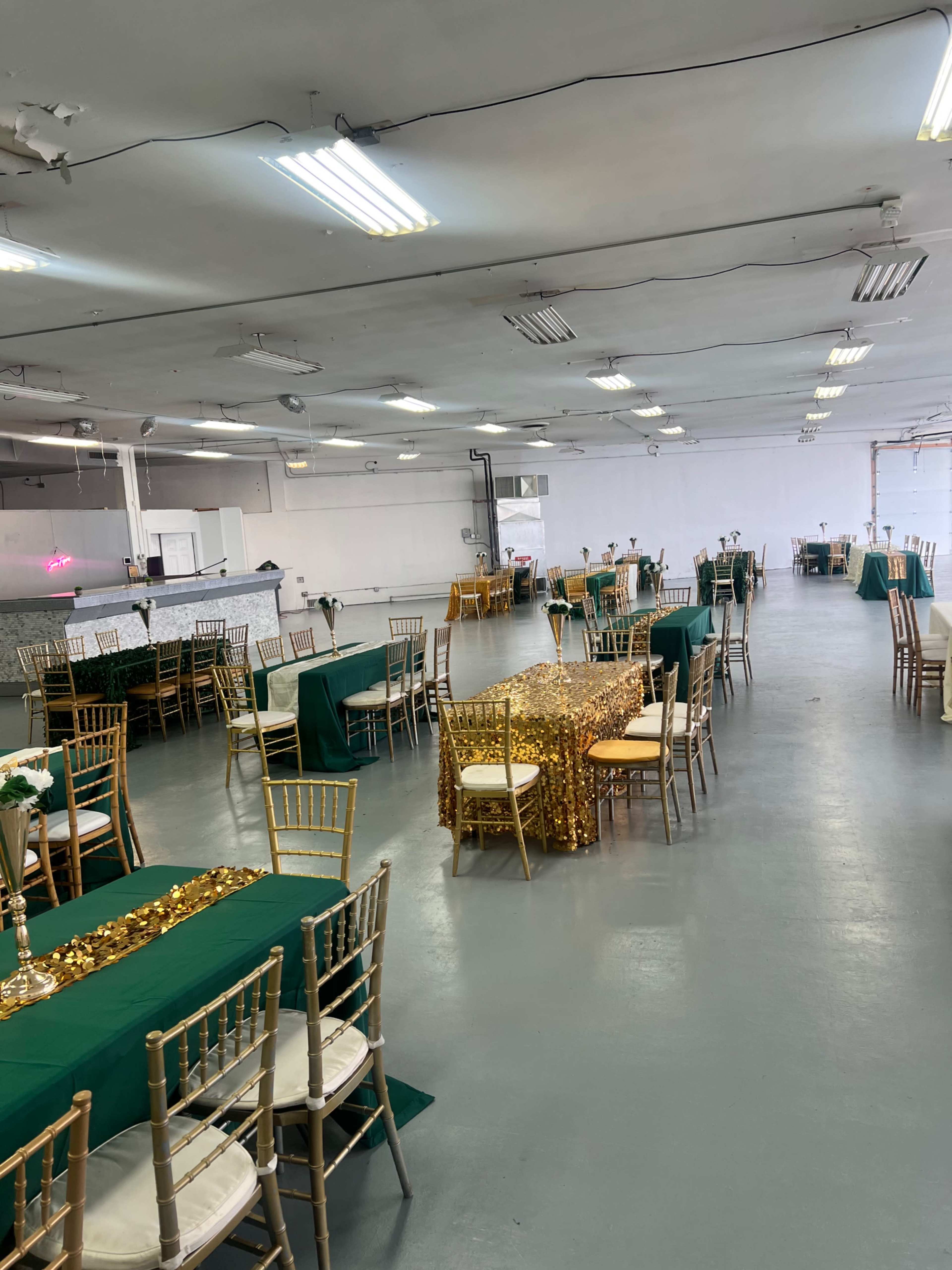 A large event space set up with multiple tables covered in green and gold decorations, arranged in rows.