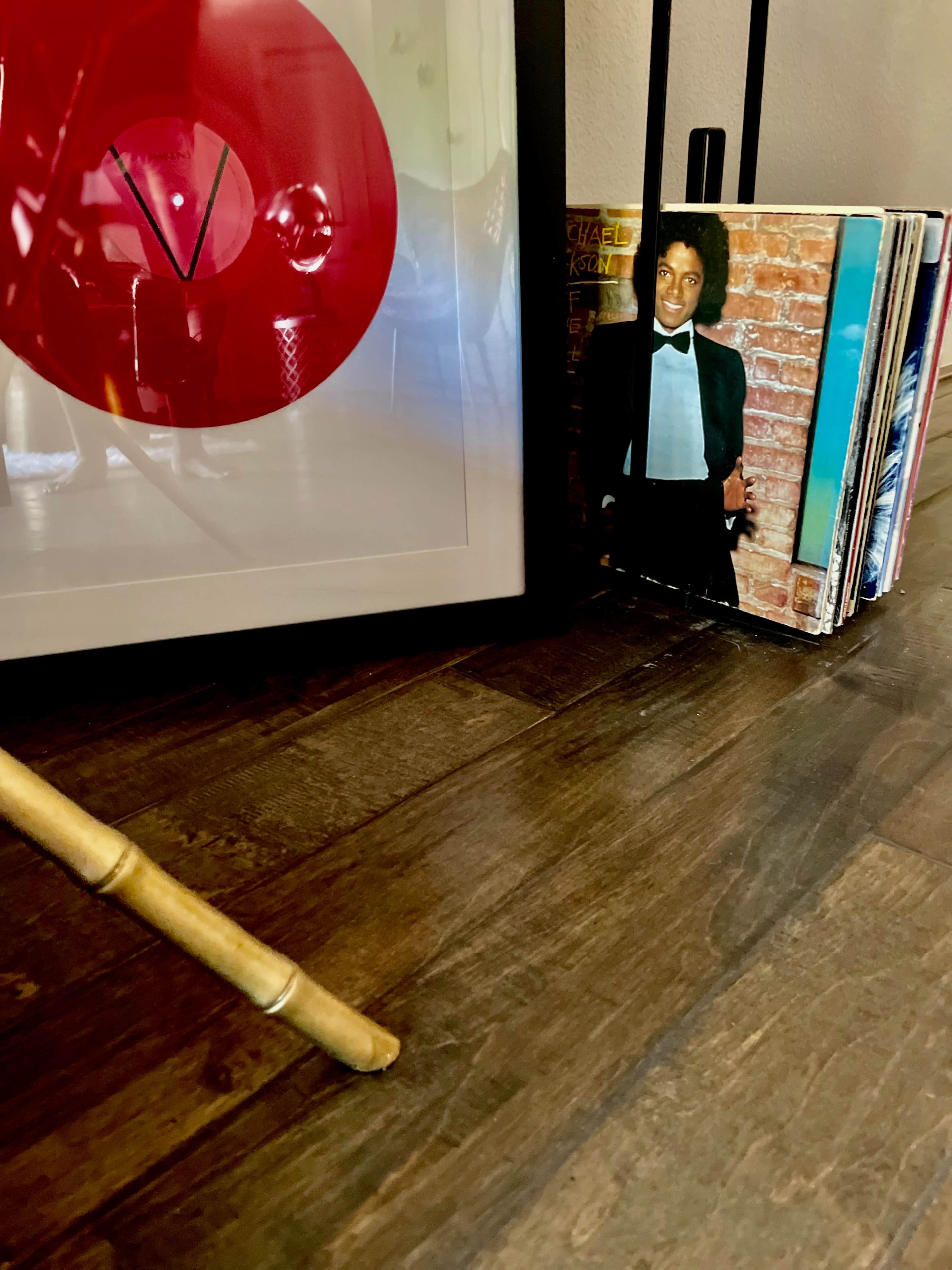 A framed photo featuring red circular designs is placed next to a stack of CDs, with a notable album cover featuring a man in a tuxedo.