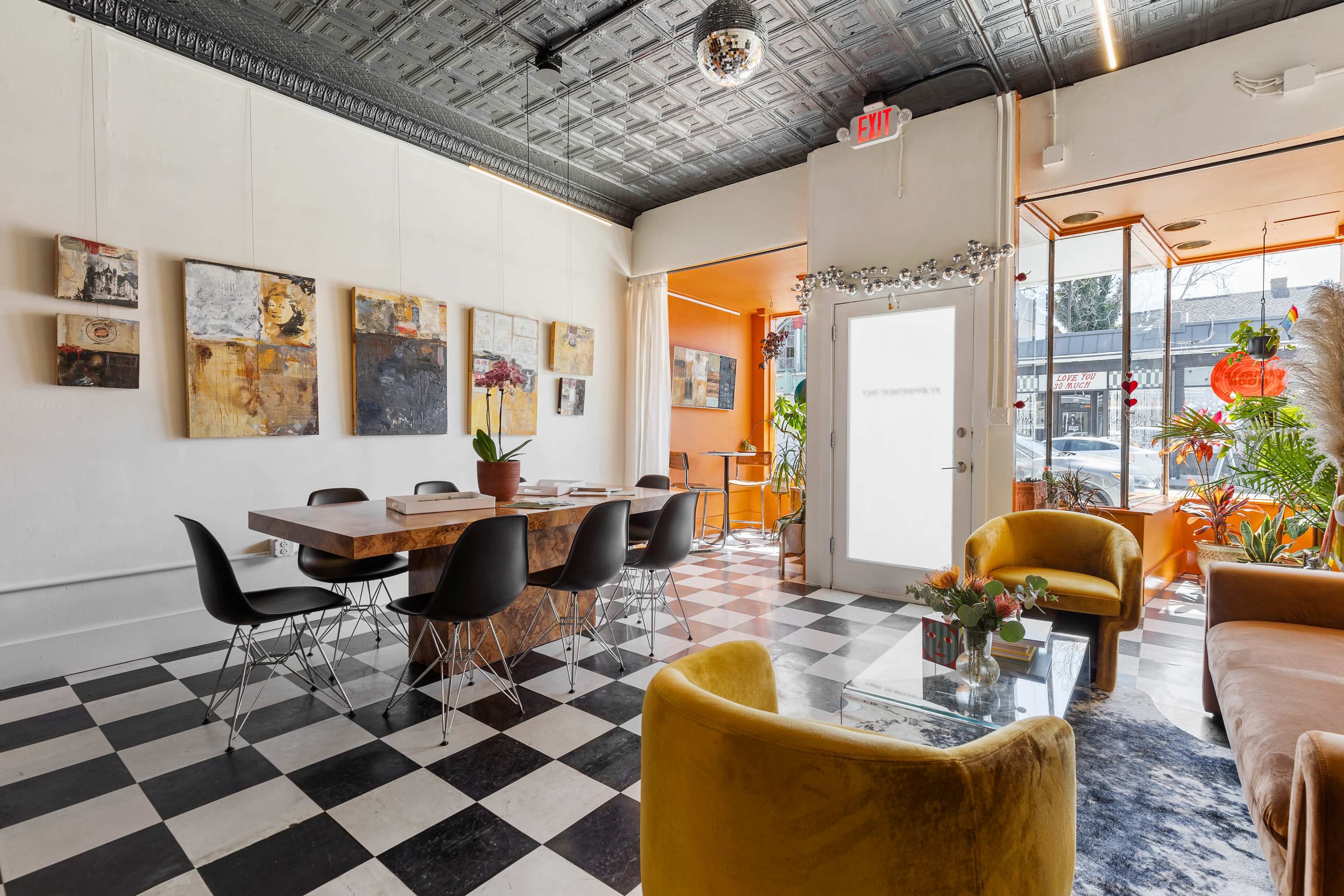 The image shows a modern café with a black and white checkered floor, a long wooden table surrounded by black chairs, and colorful artwork on the walls.