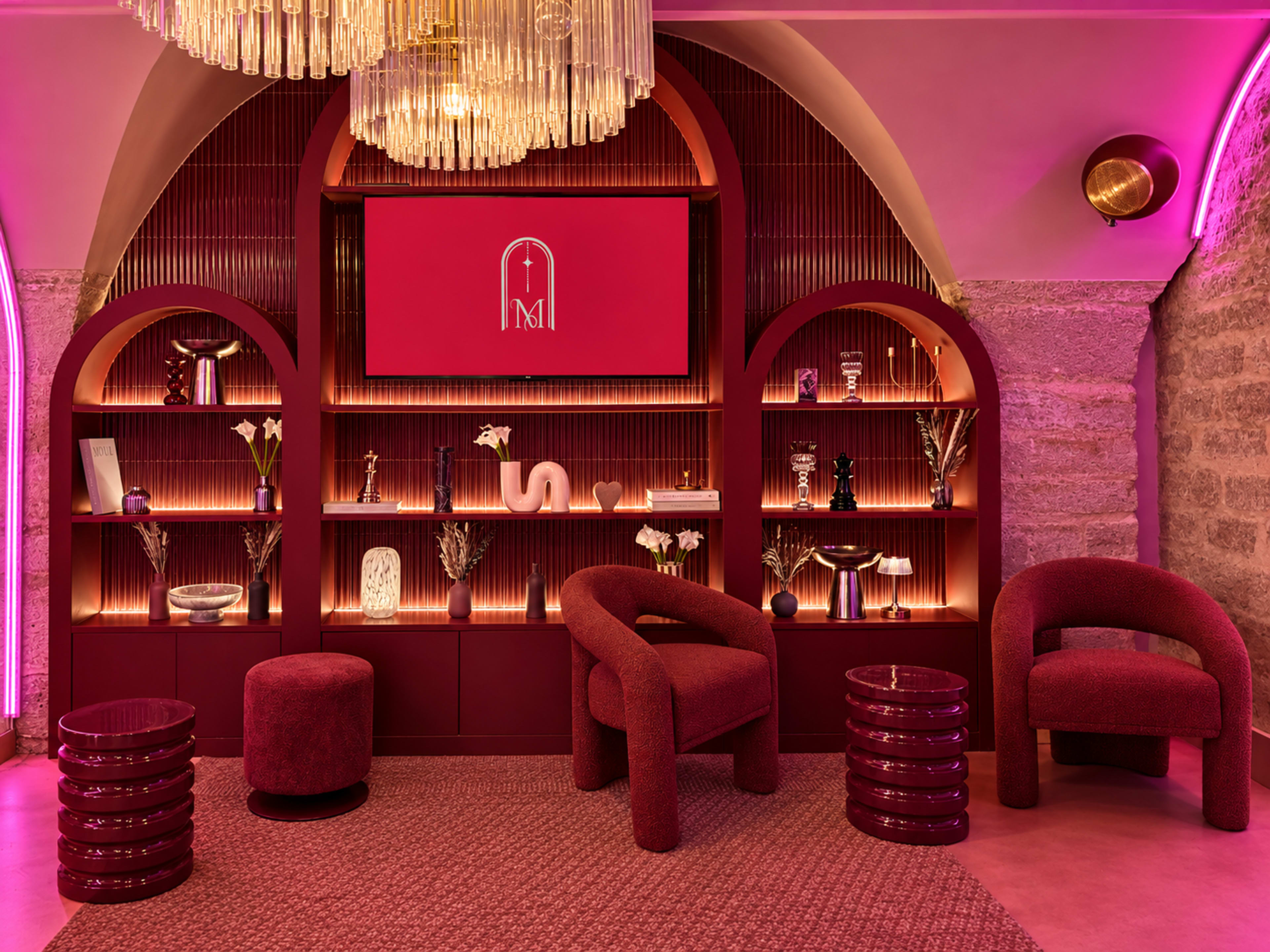 The image showcases a stylish interior featuring a burgundy shelf with various decorative items, plush seating, and ambient lighting.