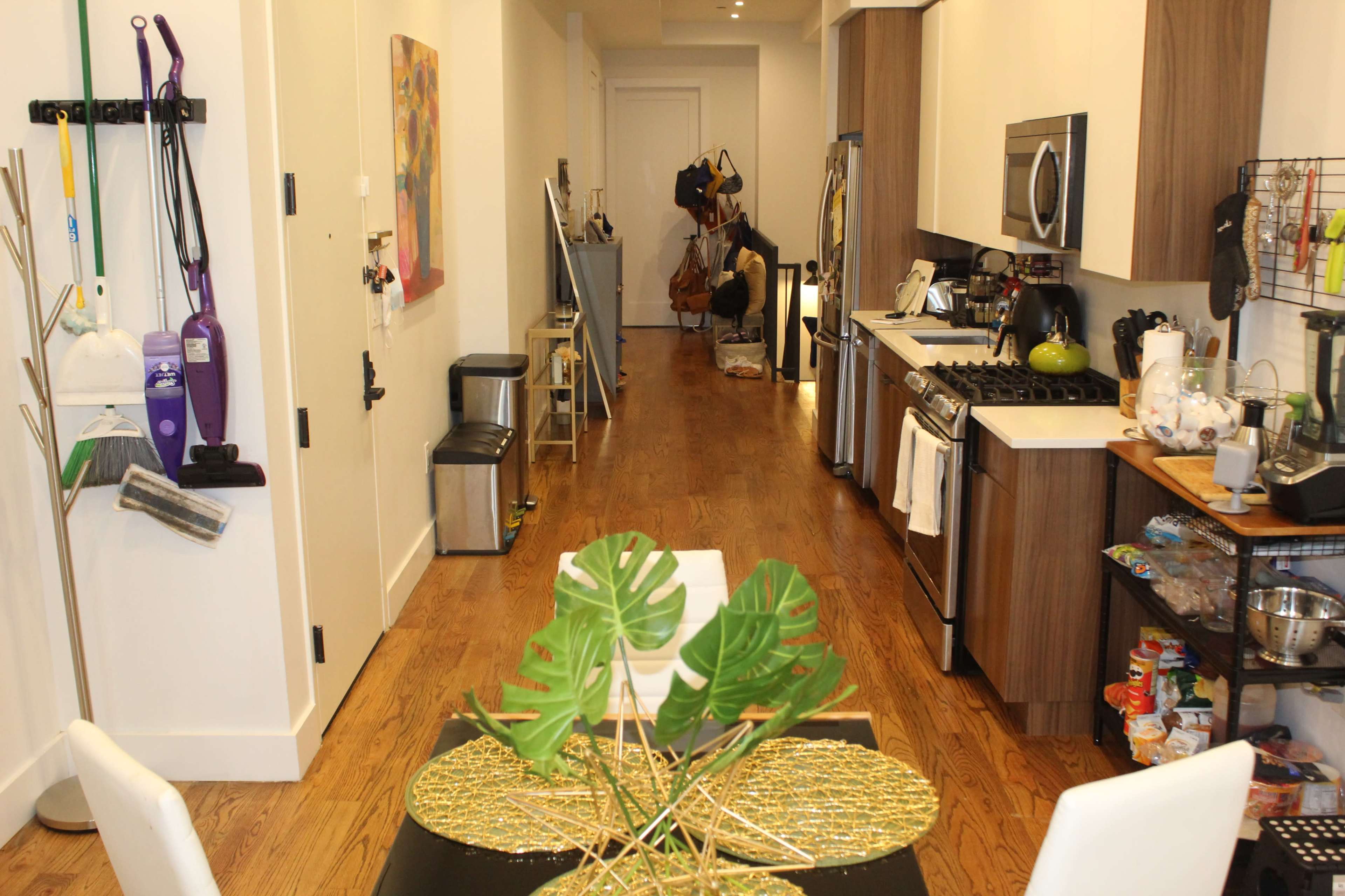 A modern kitchen and dining area with wooden floors, featuring a long hallway extending towards a door at the end.