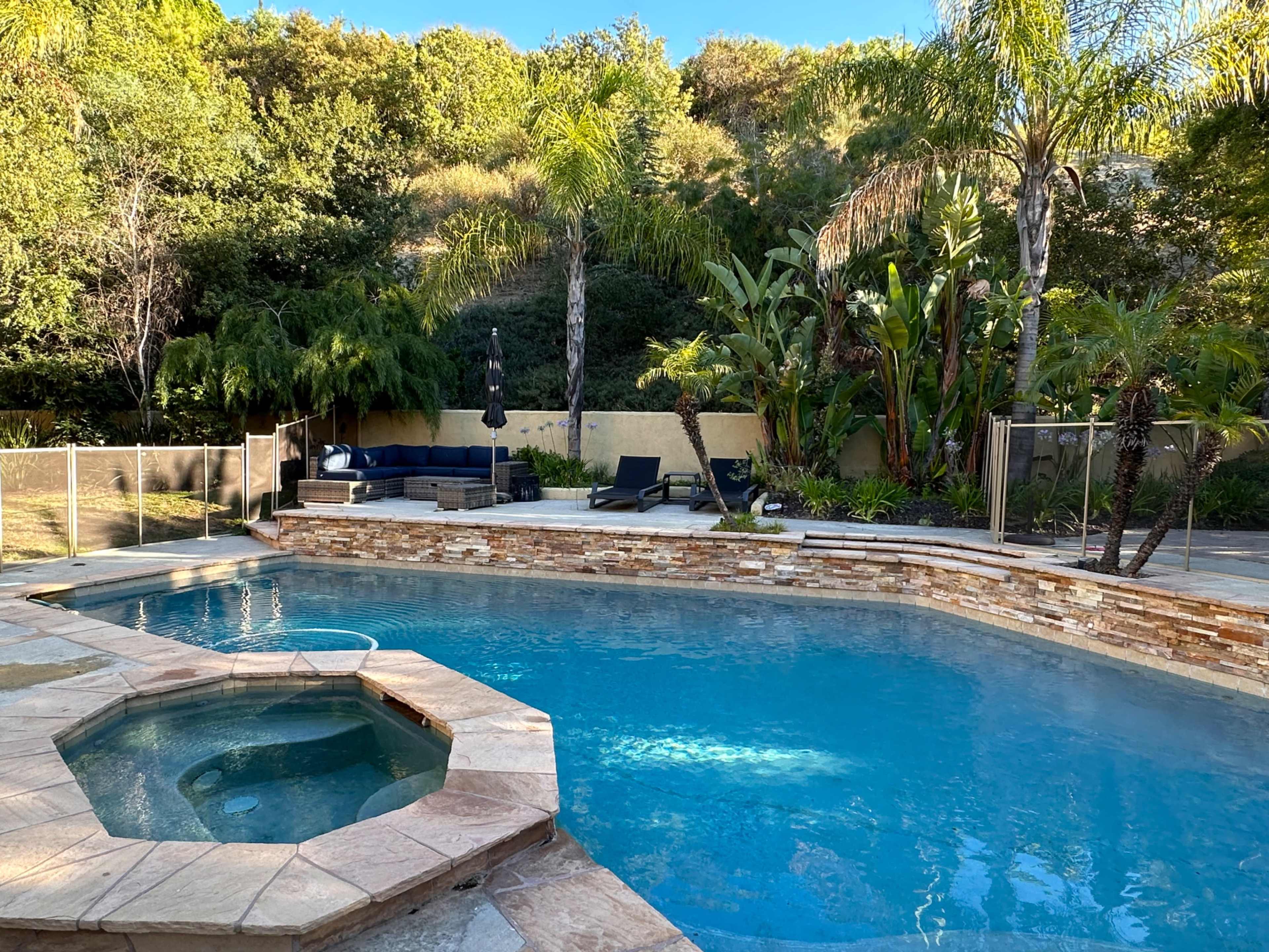 A swimming pool with a hot tub and lounge chairs surrounded by tropical landscaping.