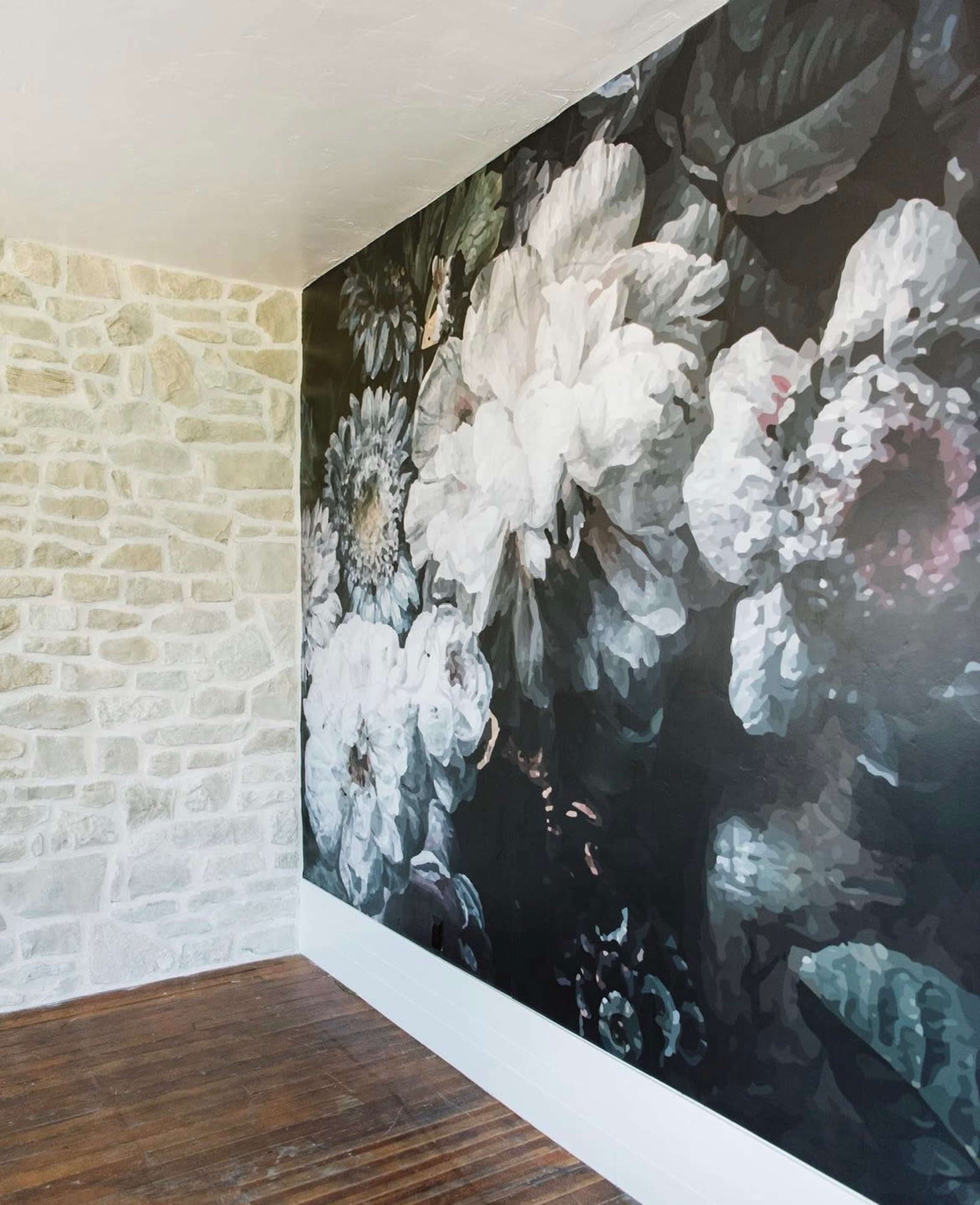A large floral mural composed of white and pastel flowers covers one wall of a room with a stone accent wall and wooden flooring.