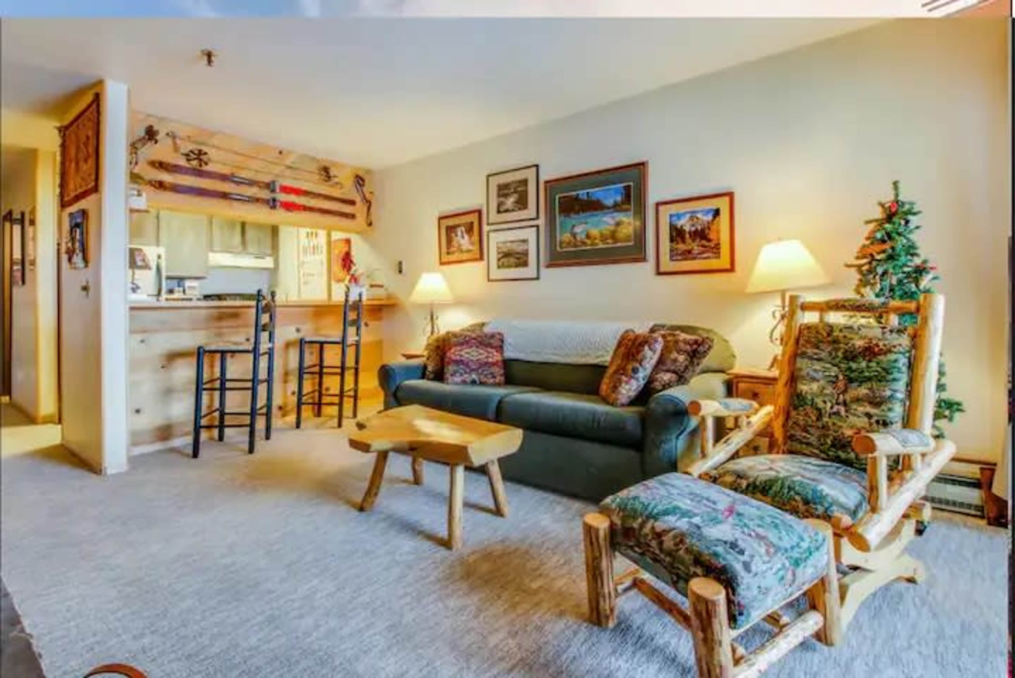 The living room features a sofa, two wooden chairs, a coffee table, and several framed pictures on the walls.