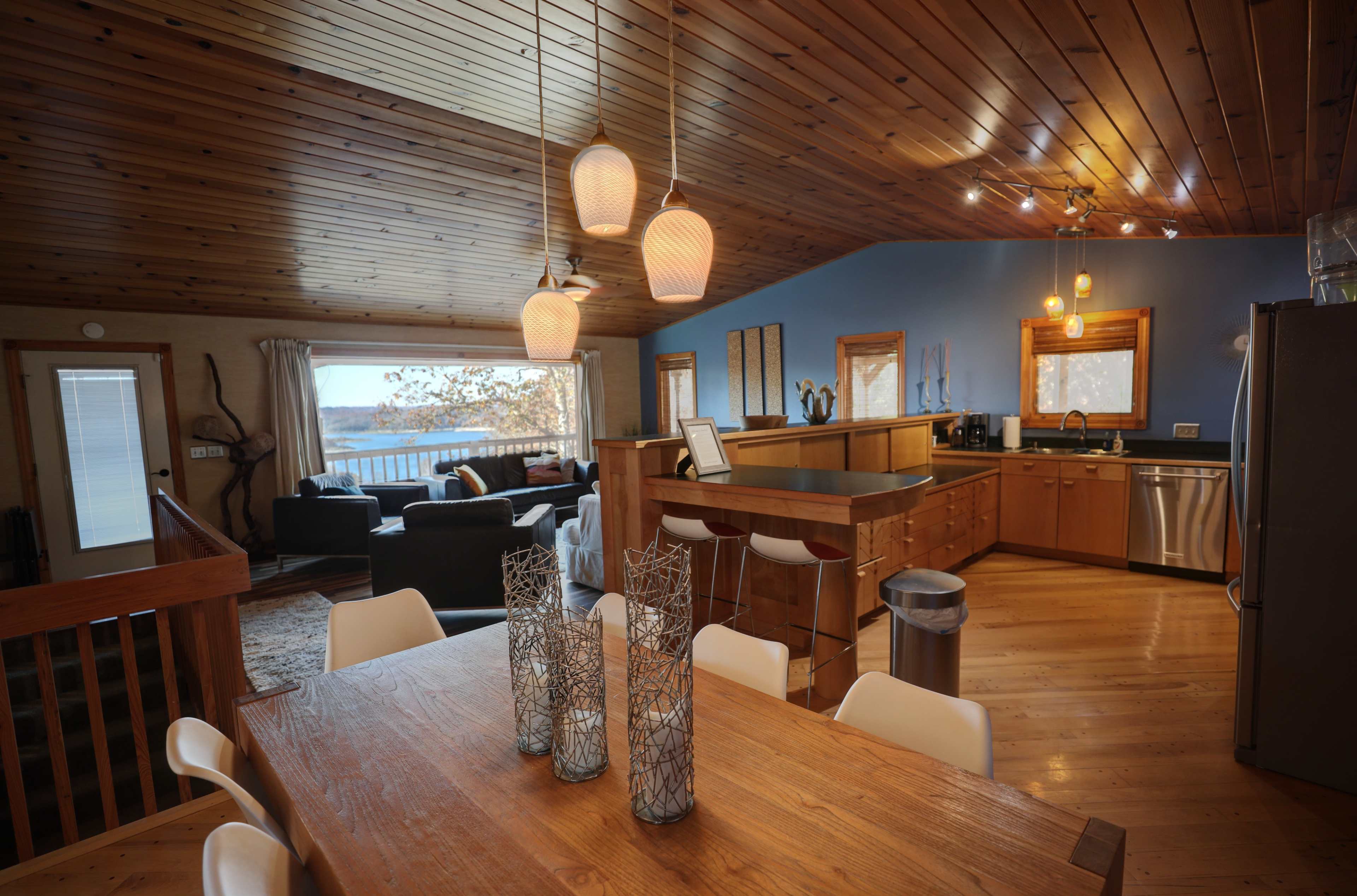A modern, open-concept living space featuring a dining table, a kitchen area, and a living room with large windows overlooking a scenic view.