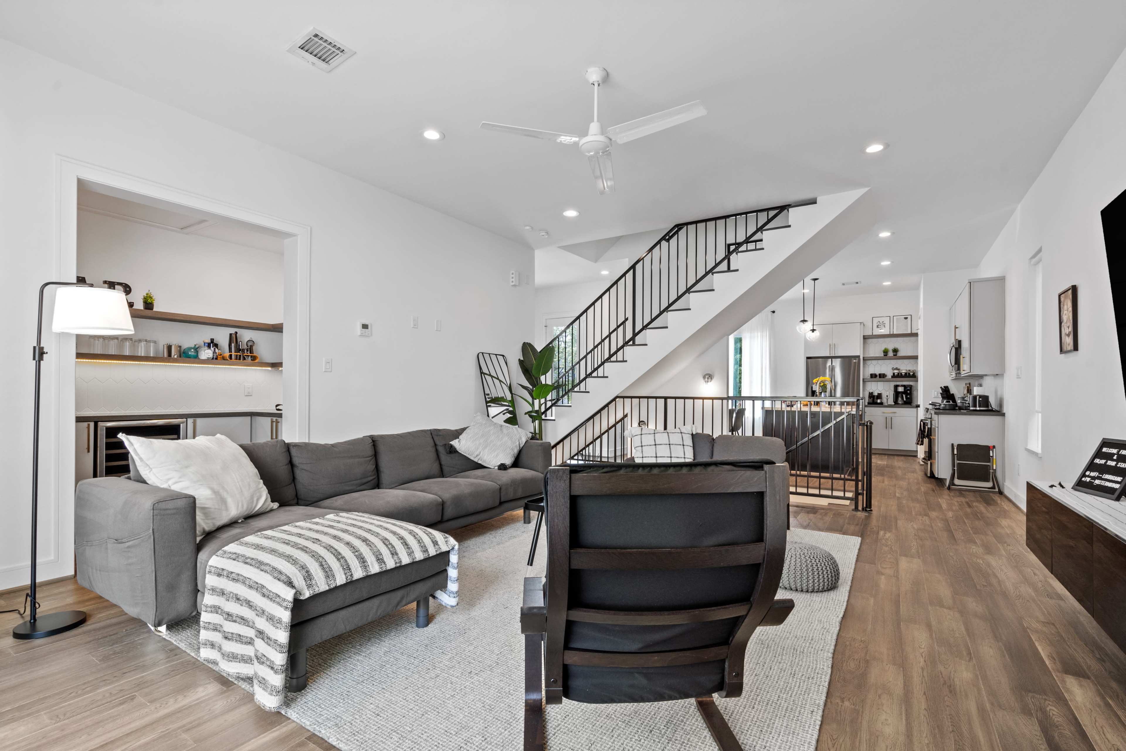 A modern living room with a sectional sofa, a chair, and a staircase leading to an upper level, all set against a backdrop of light-colored walls and hardwood flooring.
