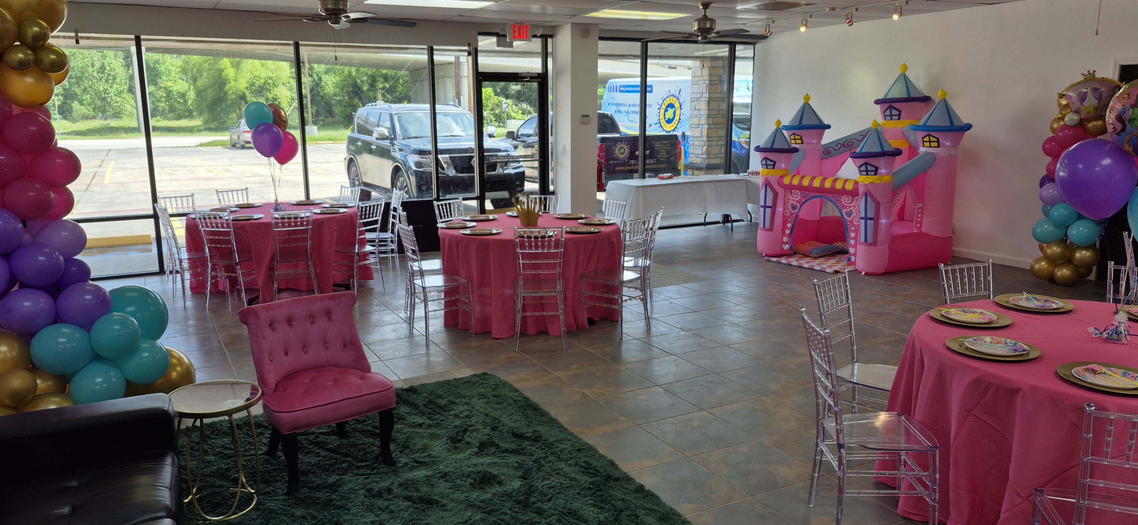 The image shows a brightly decorated party venue with pink tables, a pink bounce house, and colorful balloons.
