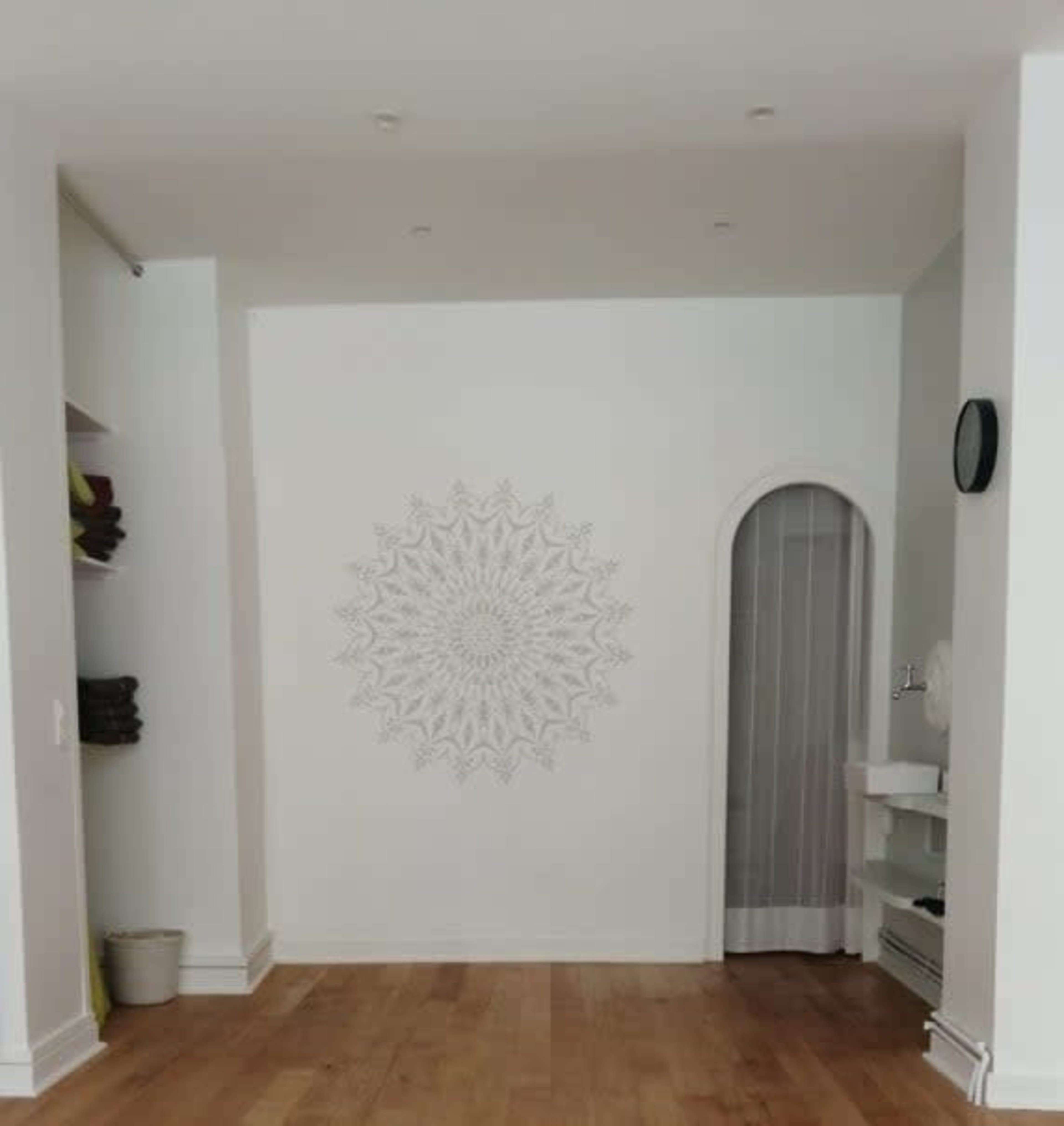 A minimalist interior space featuring a patterned wall design, a small archway, and shelves with neatly arranged towels.